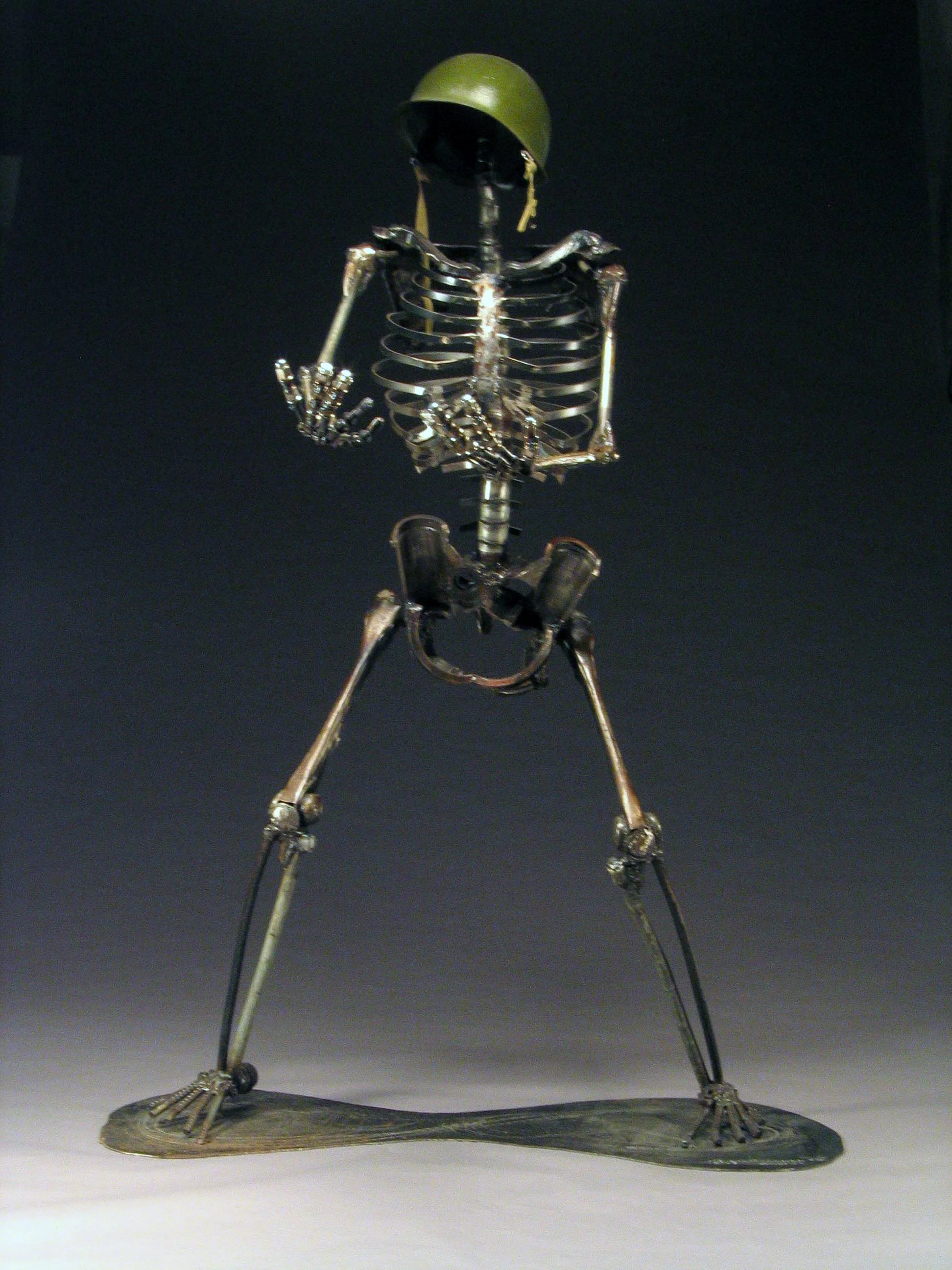 A metallic skeleton sculpture in a running pose, wearing a military helmet, with a black background.