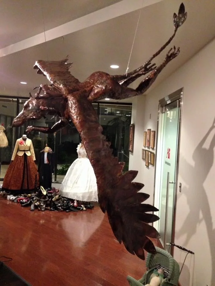 Large wooden sculpture of a whale with a splash, displayed indoors with mannequins and clothing in the background.