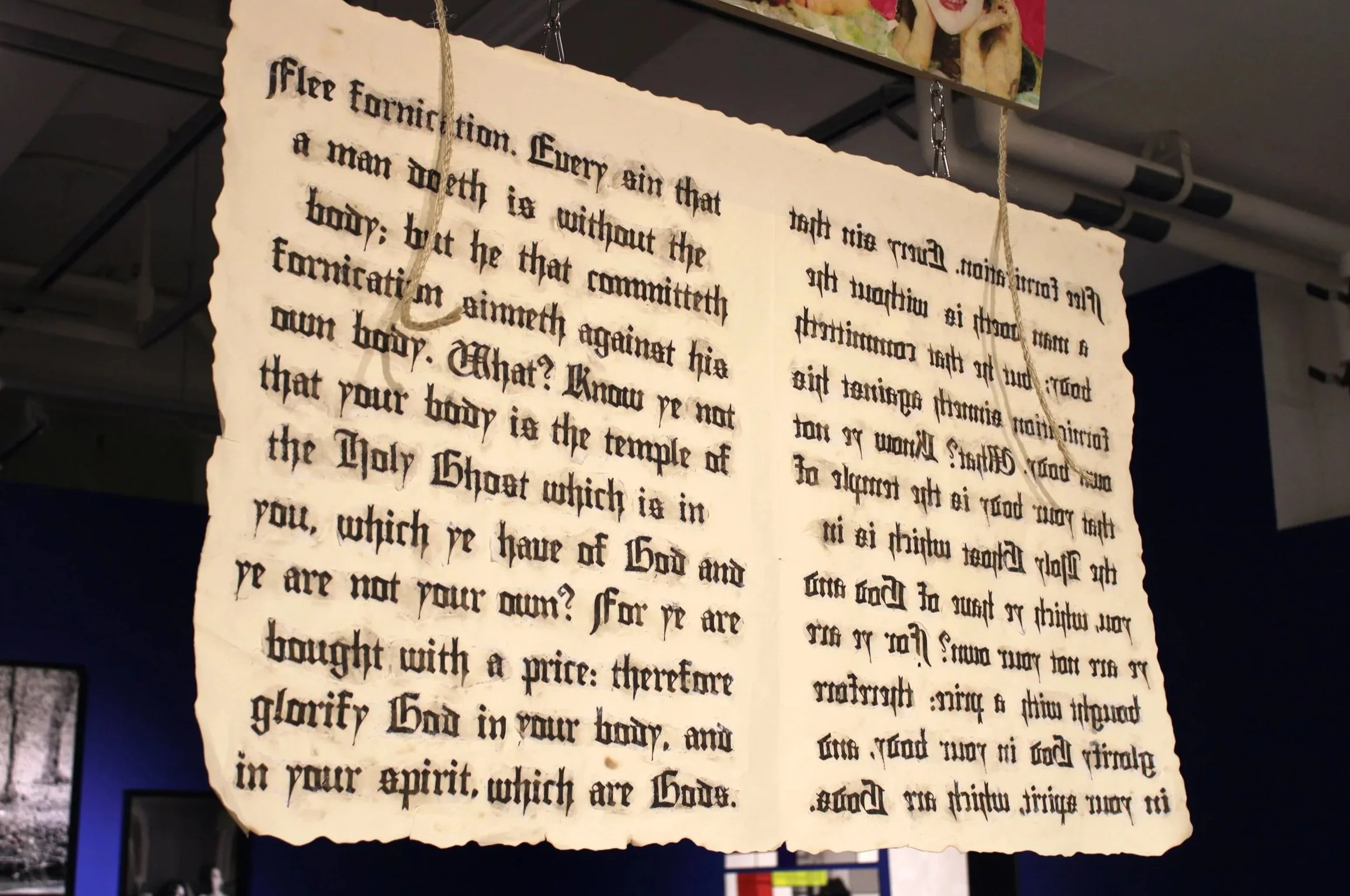 A torn piece of parchment with handwritten text, hanging from chains in a display.