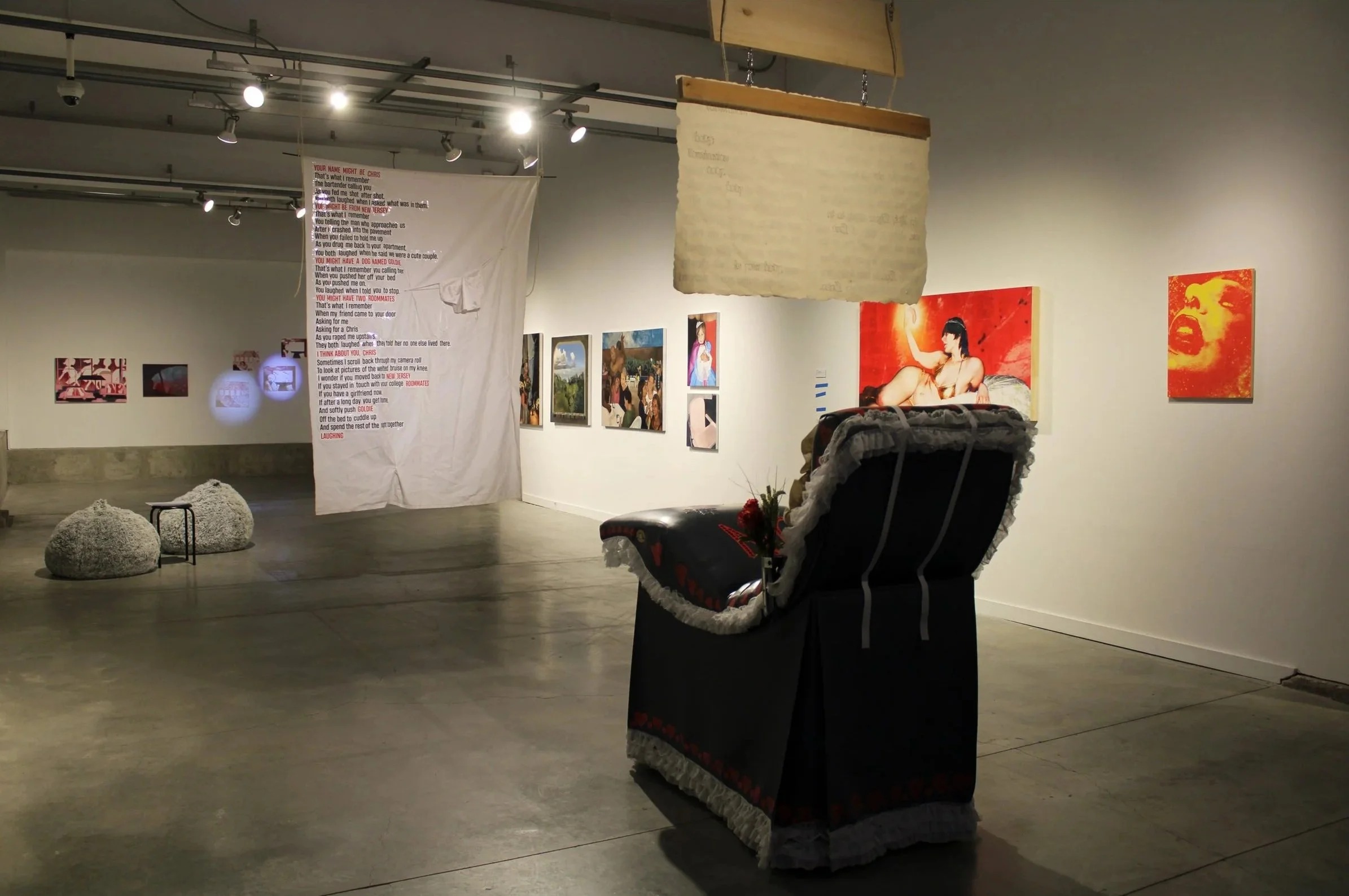 View of an art gallery with paintings on the wall, a hanging fabric with text, and a wheelchair in the foreground.