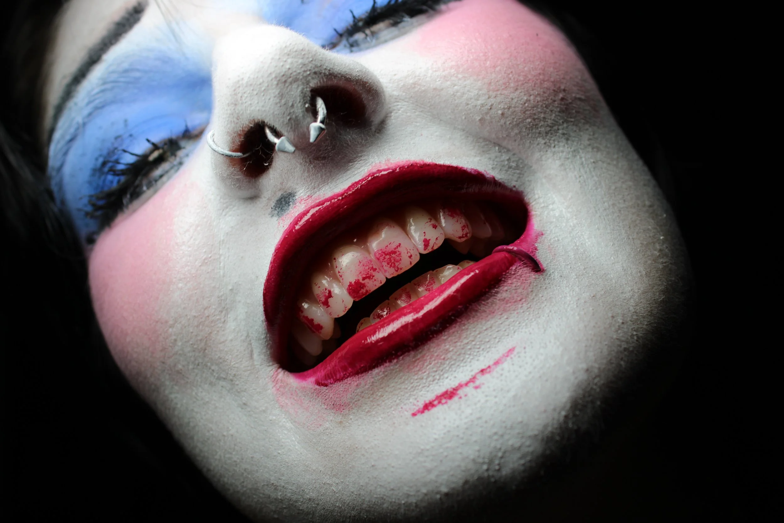 Close-up of a smiling personwith makeup, bright red lipstick, and nose piercings.