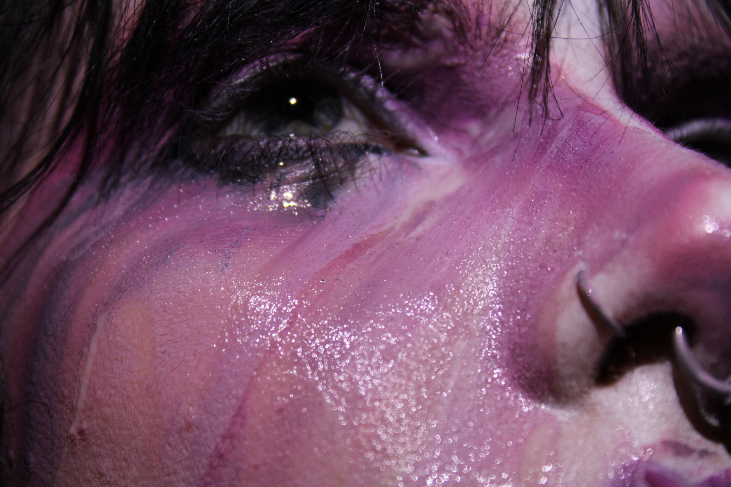 Close-up of a person's eye with makeup, showing black eyeliner and sparkly eyeshadow, along with wet skin and dark hair strands.