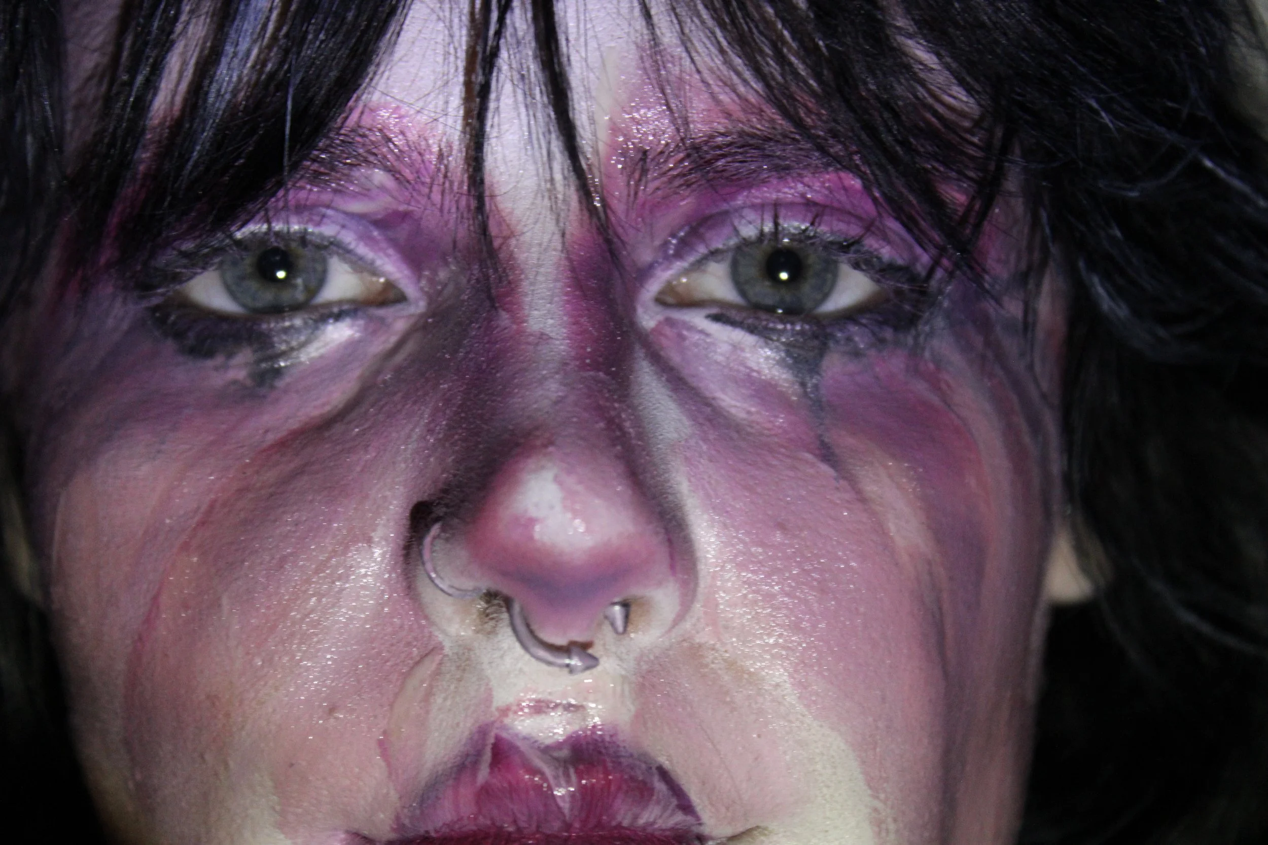 Close-up of a person with dramatic makeup, black hair, and piercings on their nose, with glitter on their eyelids and lips.