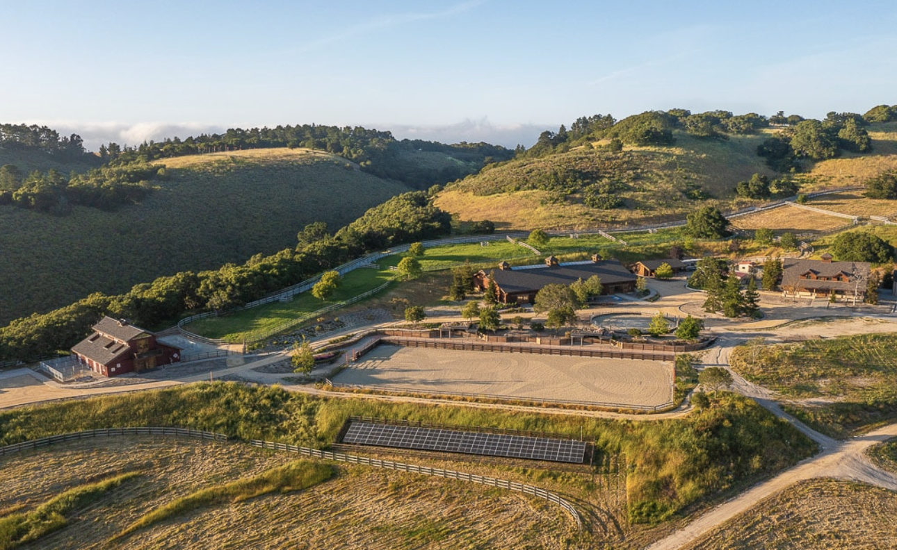 A large ranch property in Carmel, California, complete with four equestrian buildings situated on rolling green hills.