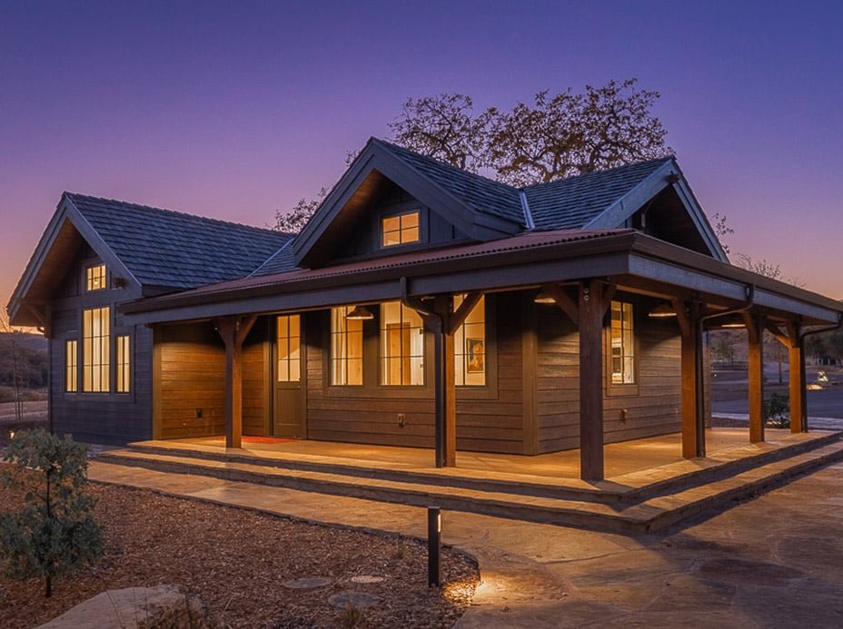 A modern post and beam cabin designed with grey siding and a stone walkway.
