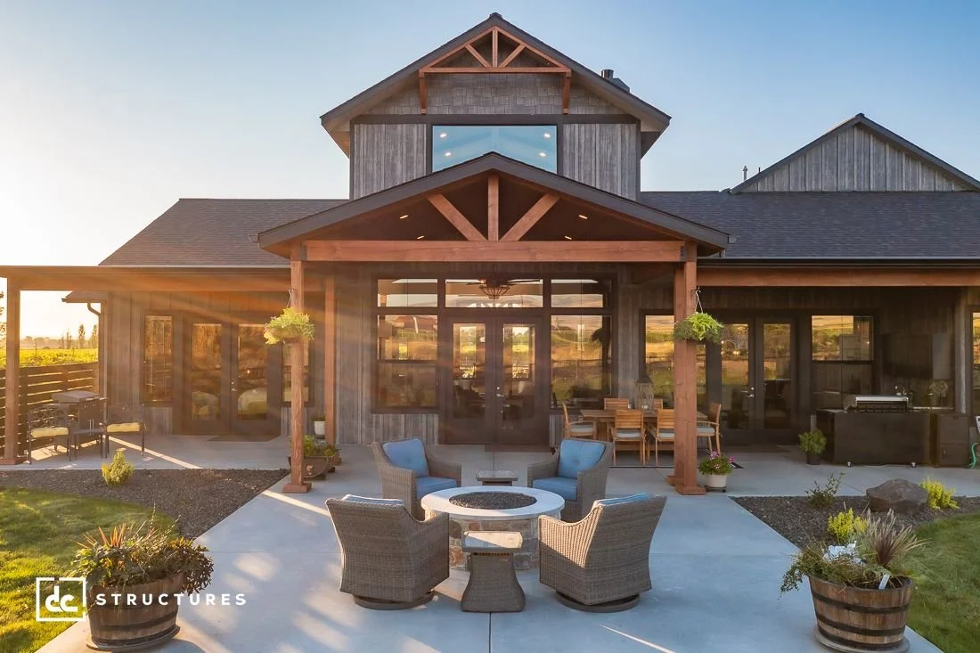 A modern farmhouse with grey vertical siding, wood beams ad posts, and a spacious outdoor living space.