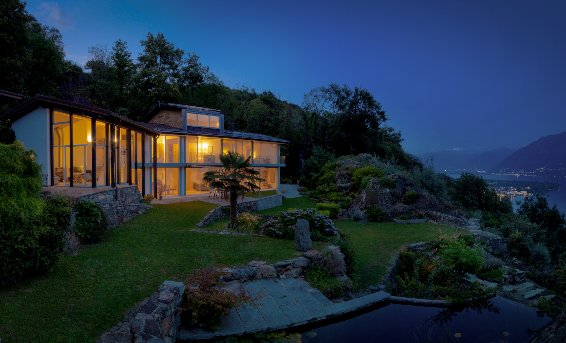 Luxury hillside home at dusk with floor-to-ceiling glass windows and warm interior glow