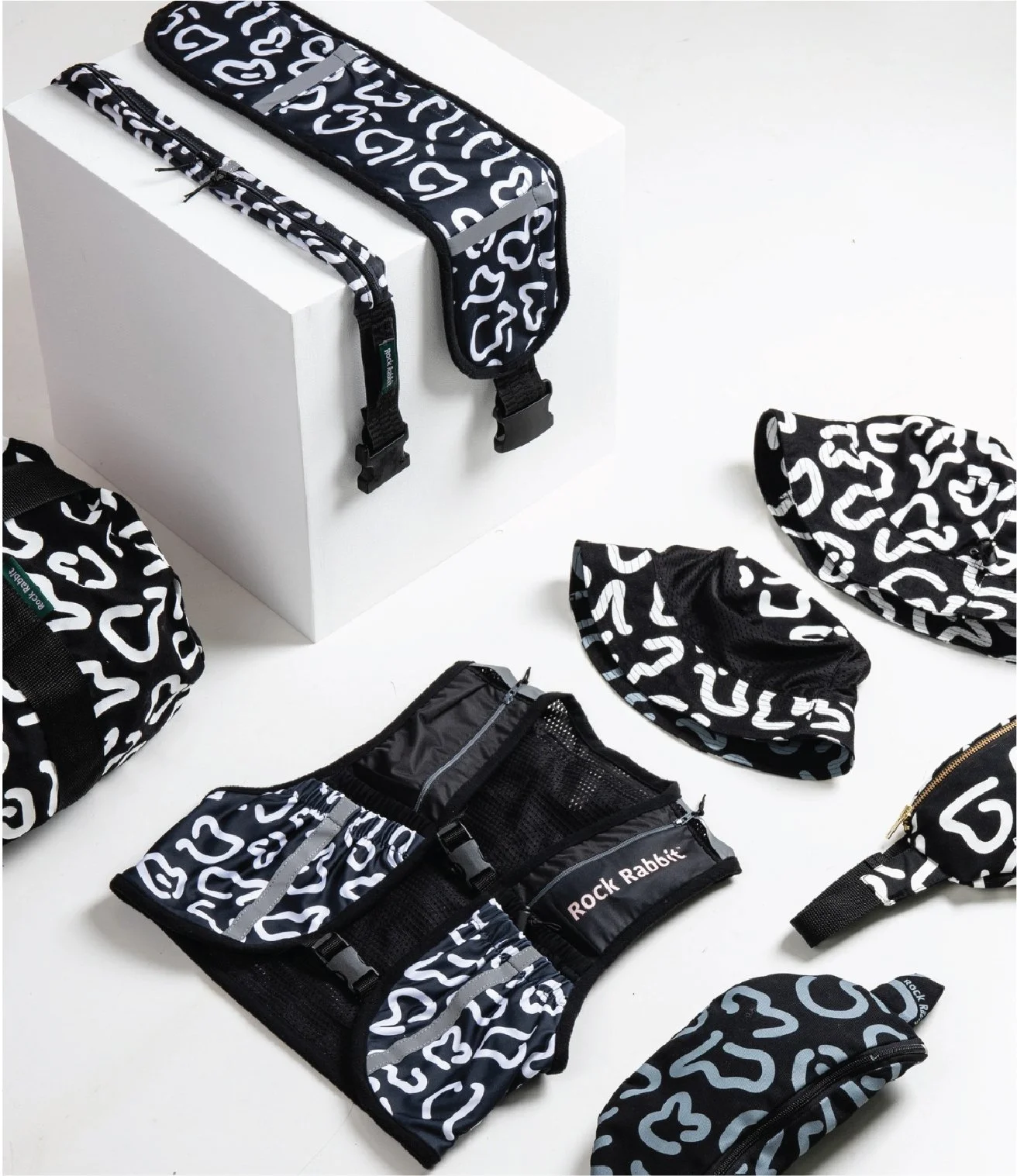 Collection of black and white patterned trail running gear accessories, including water belts, bucket hats, and hydration vests, moonbags, arranged on a white surface with a white box in the background. I designed the textile for these products