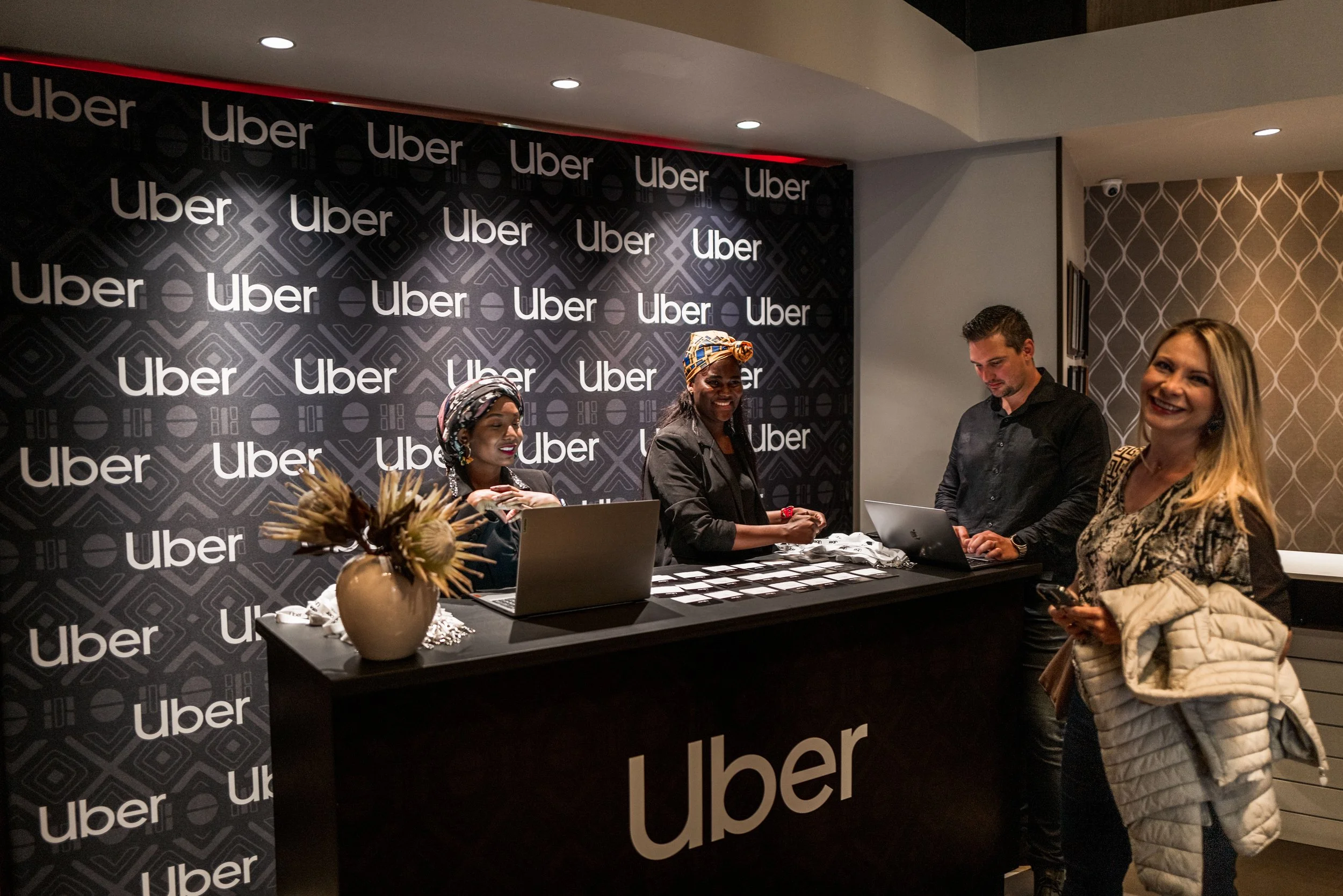 People at an Uber event registration desk with a black backdrop displaying the Uber logo repeatedly.