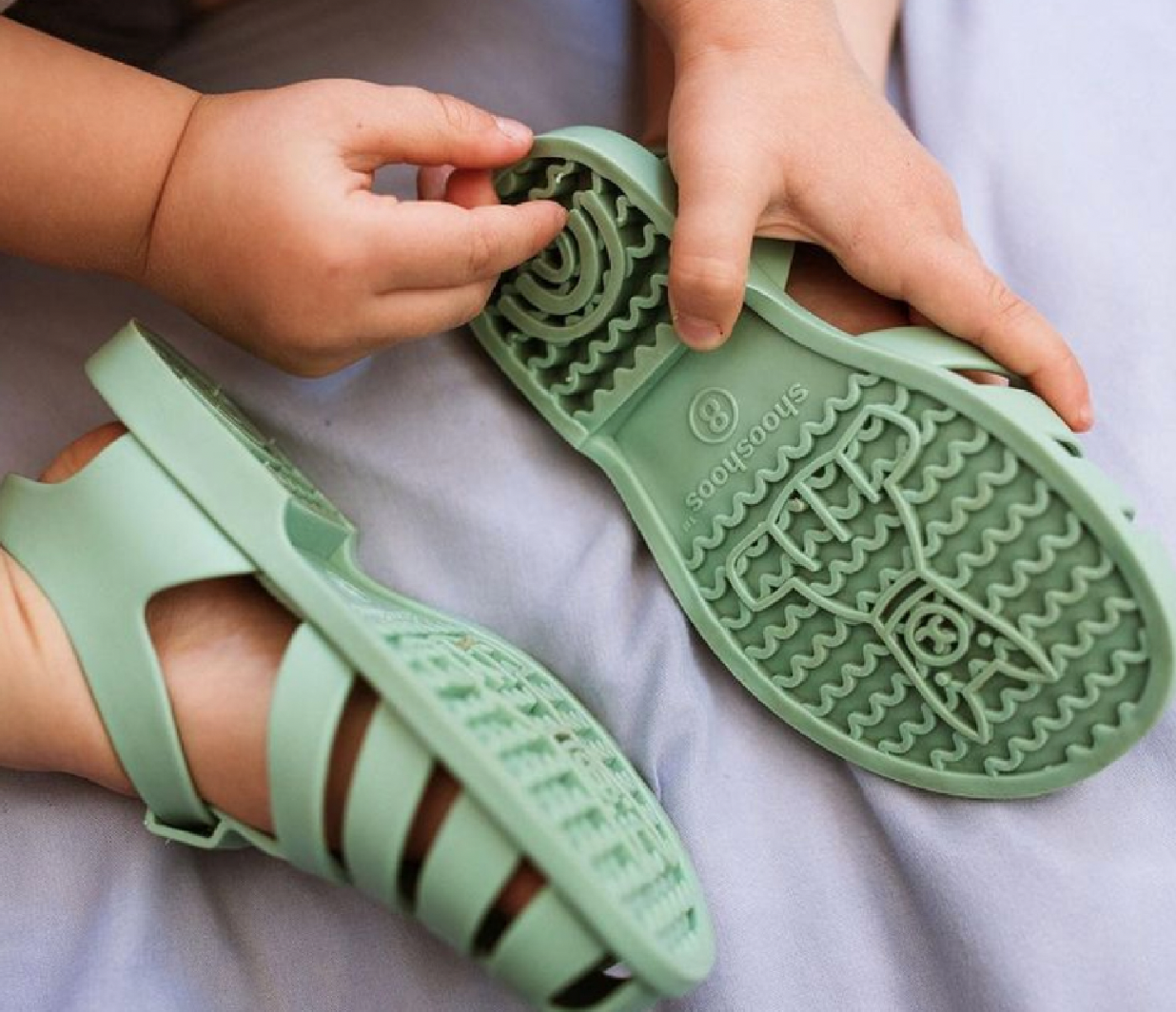 A child holding the sole of a green rubber sandal, with another sandal in the foreground, both with patterned soles with a lama graphic which I created.