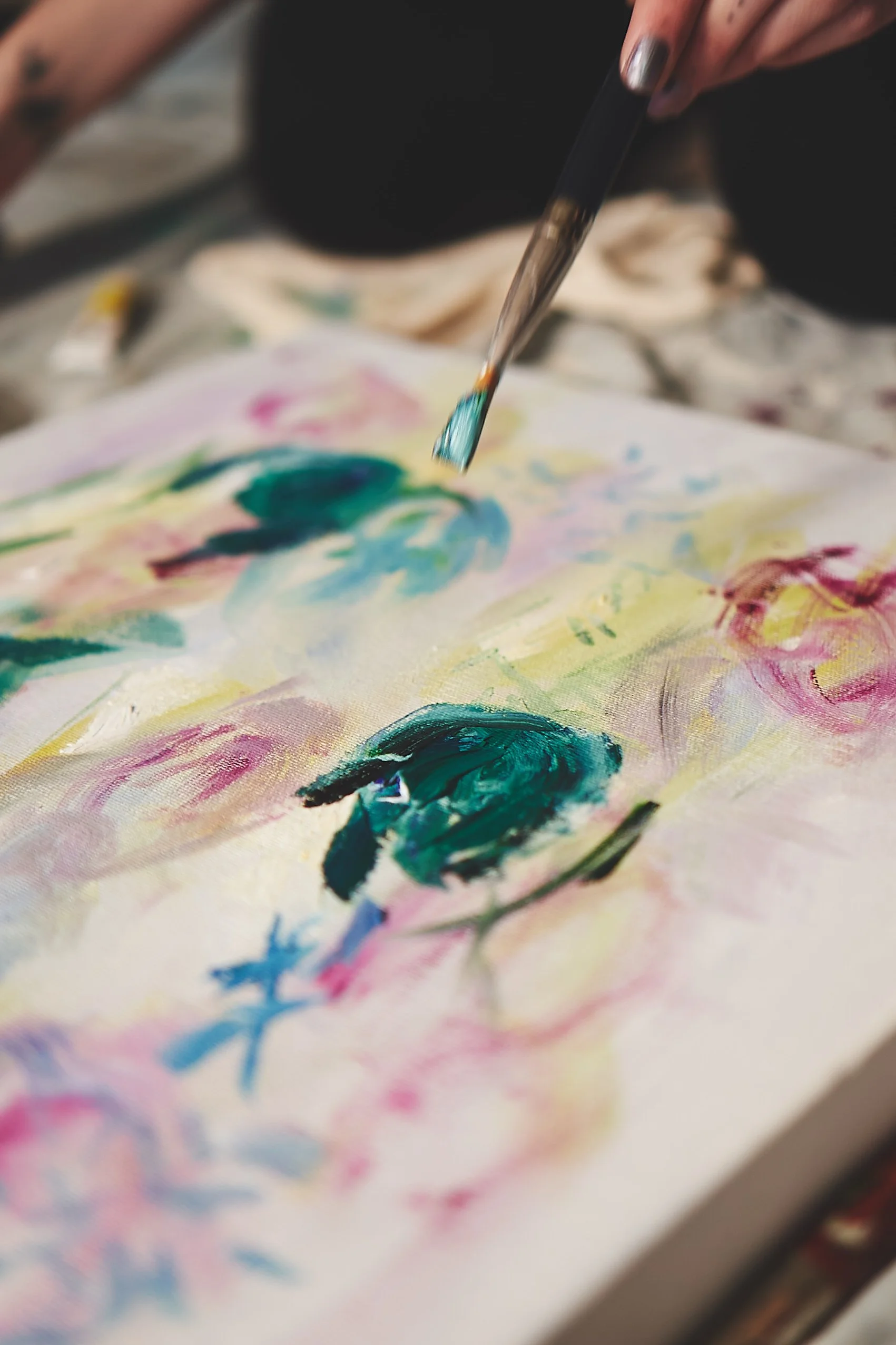 Close-up of a hand holding a paintbrush with vibrant, colorful paint strokes on a canvas.