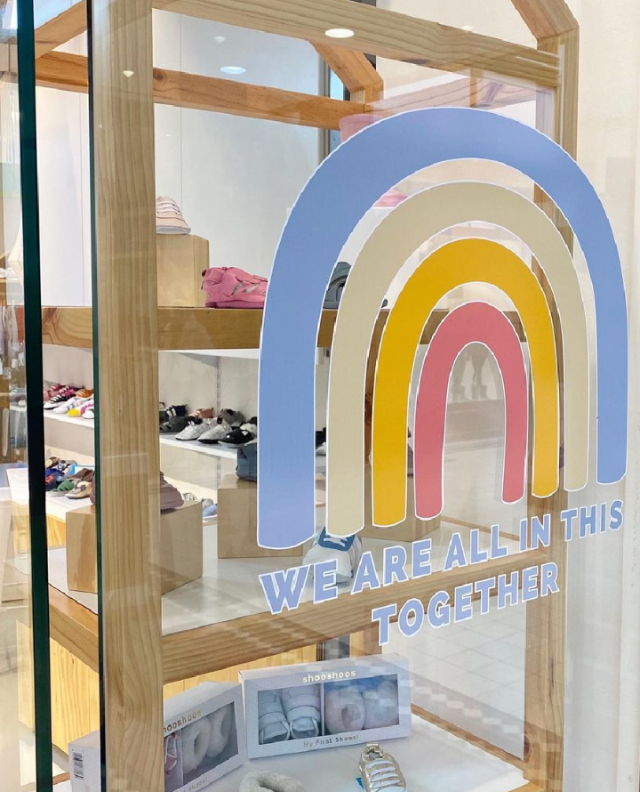 Store window display with a colorful rainbow graphic and the phrase "We are all in this together." I designed the window vinyl for the store at the Waterfront in Cape Town, South Africa.