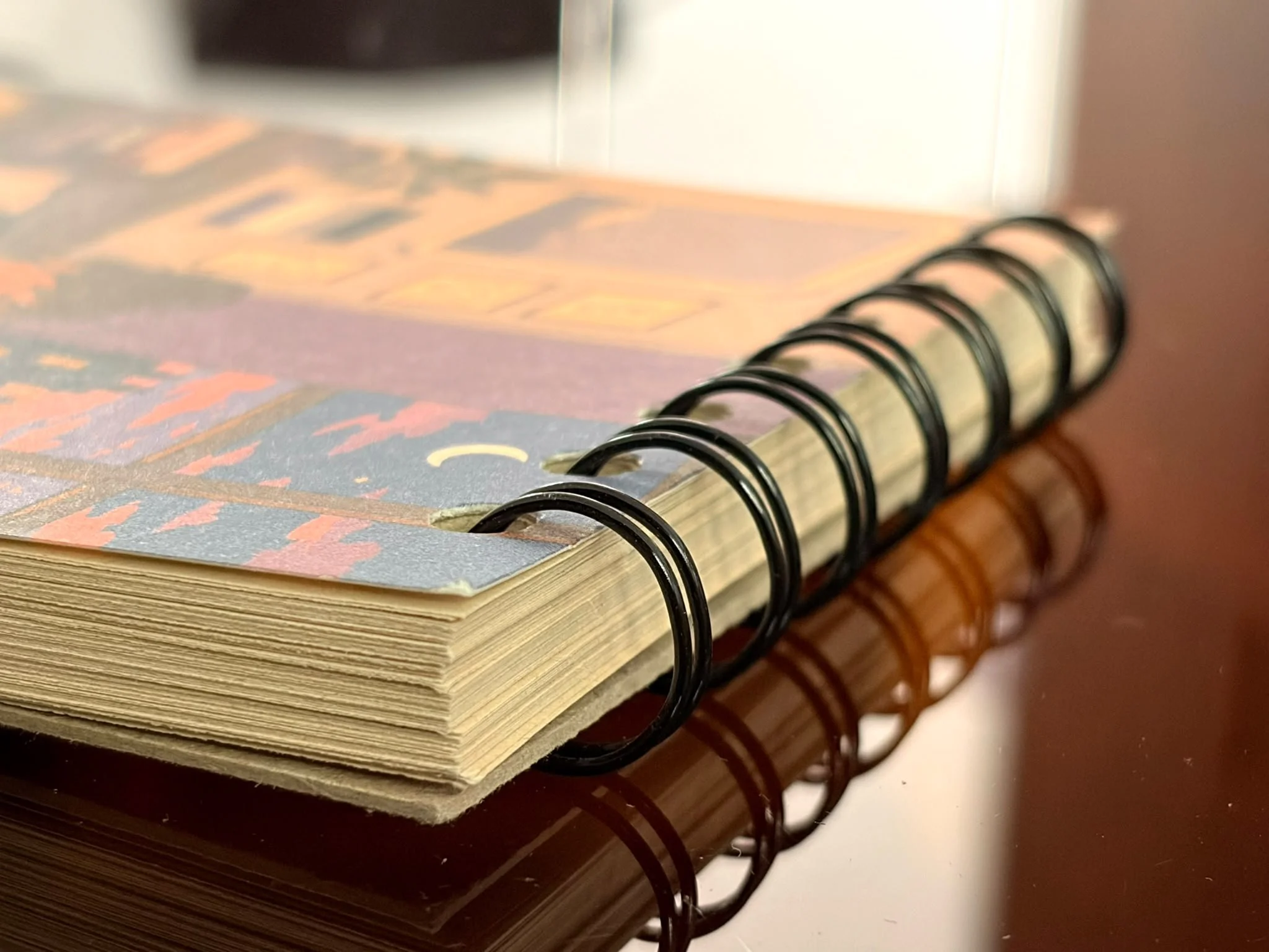 Close-up of a spiral-bound notebook with pages featuring colorful abstract designs, sitting on a dark wooden surface.