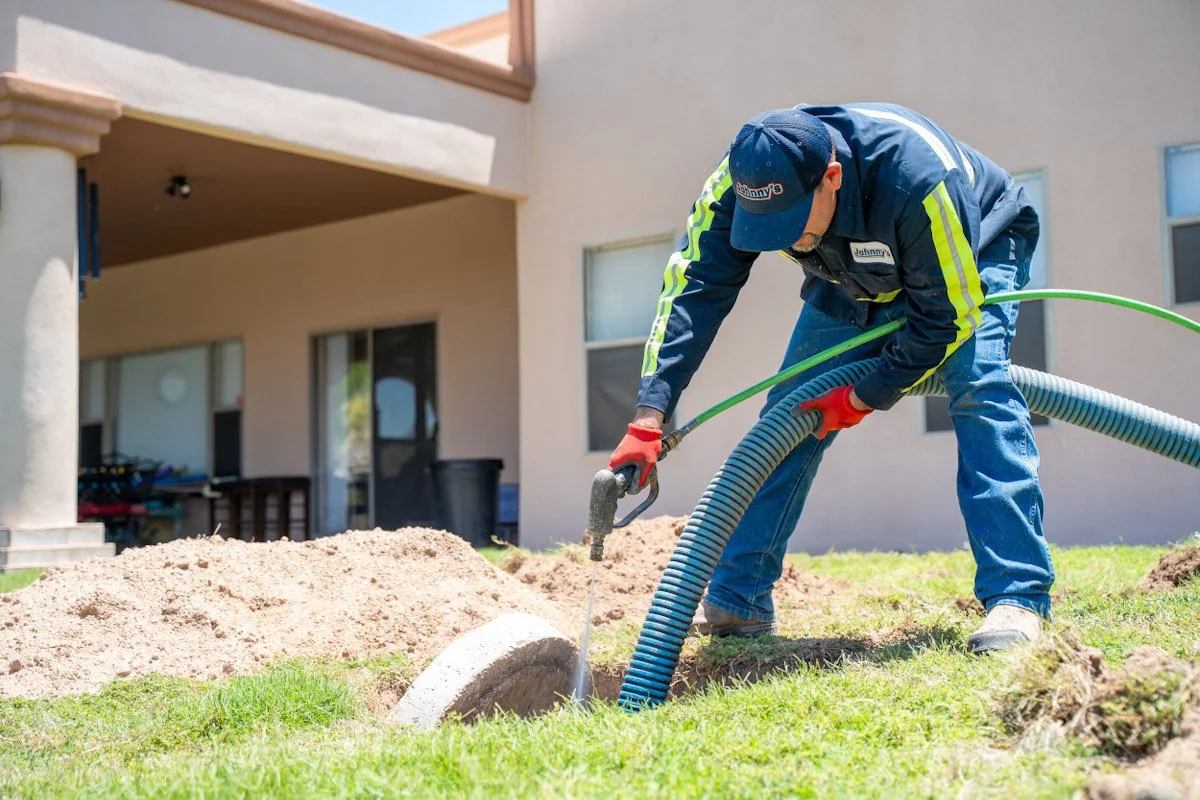 A worker with a cap, jacket, and gloves is using a wet saw to cut a concrete pipe while laying drainage pipes outside a building.