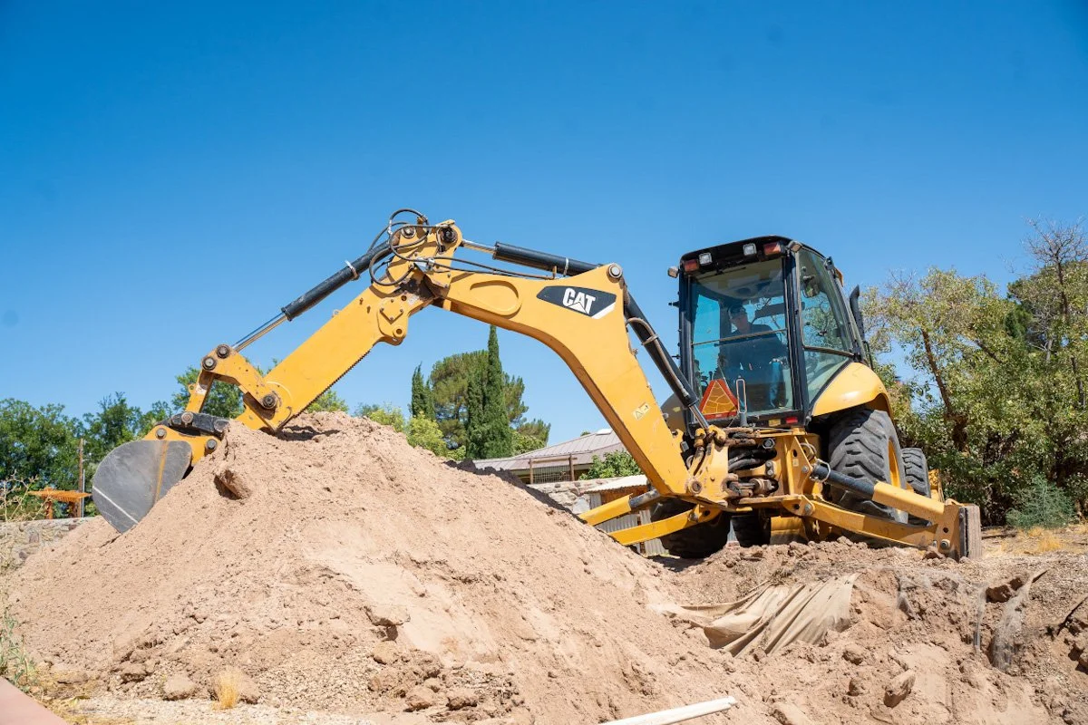 A yellow Caterpillar excavator operating on a construction site with a pile of dirt in front, under a clear blue sky.