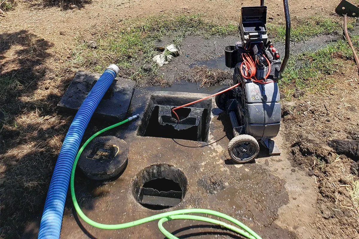 A sewer camera inspection setup with a robotic crawler and hoses near underground sewer access points.