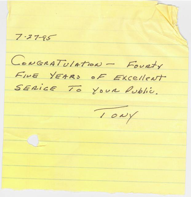 A yellow notepad paper with a handwritten note that reads: '7-27-95, Congratulations - Forty Five Years of Excellent Service to Your Public. / Tony'. The paper is slightly torn at the top right corner and has a small tear near the bottom left.