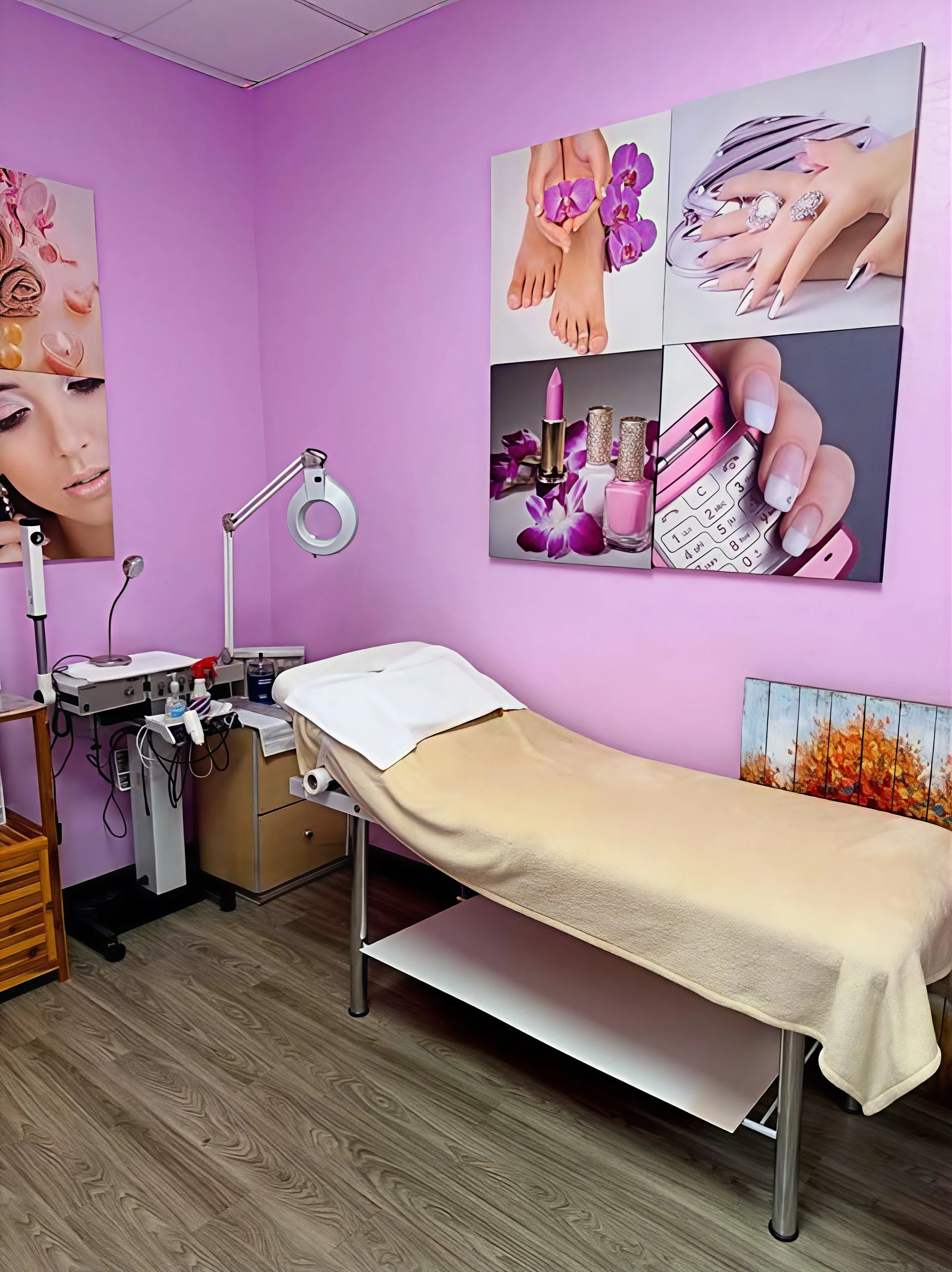 A medical examination room with pink walls and divided into sections. There is a beige exam table covered with a disposable sheet, a wooden cabinet, and a medical lamp attached to the wall. Large colorful posters depicting fashion and beauty items, like jewelry, makeup, and manicured nails, adorn the walls.