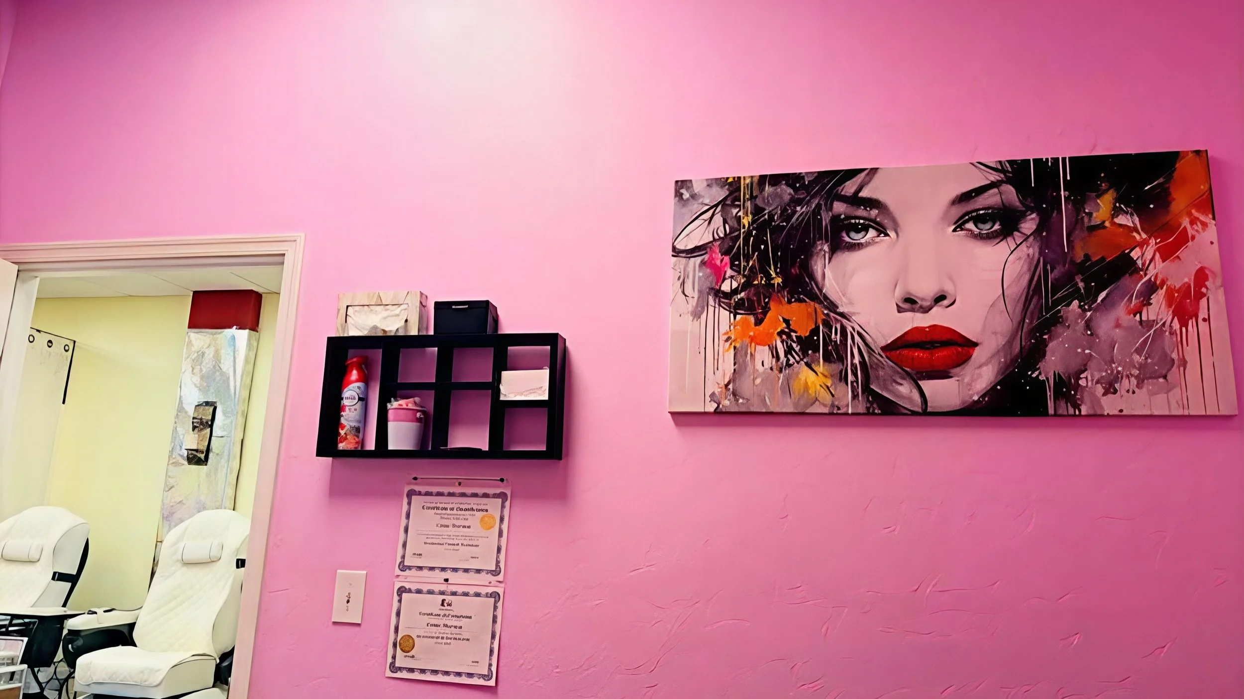 A pink wall in a salon with a large portrait of a woman with dark hair, red lips, and colorful abstract background. There are chairs, a black shelf with items, and certificates hanging on the wall.