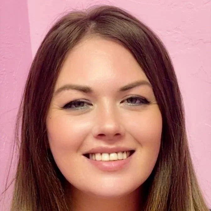 Close-up of a woman with straight, shoulder-length brown hair, fair skin, smiling against a pink background.