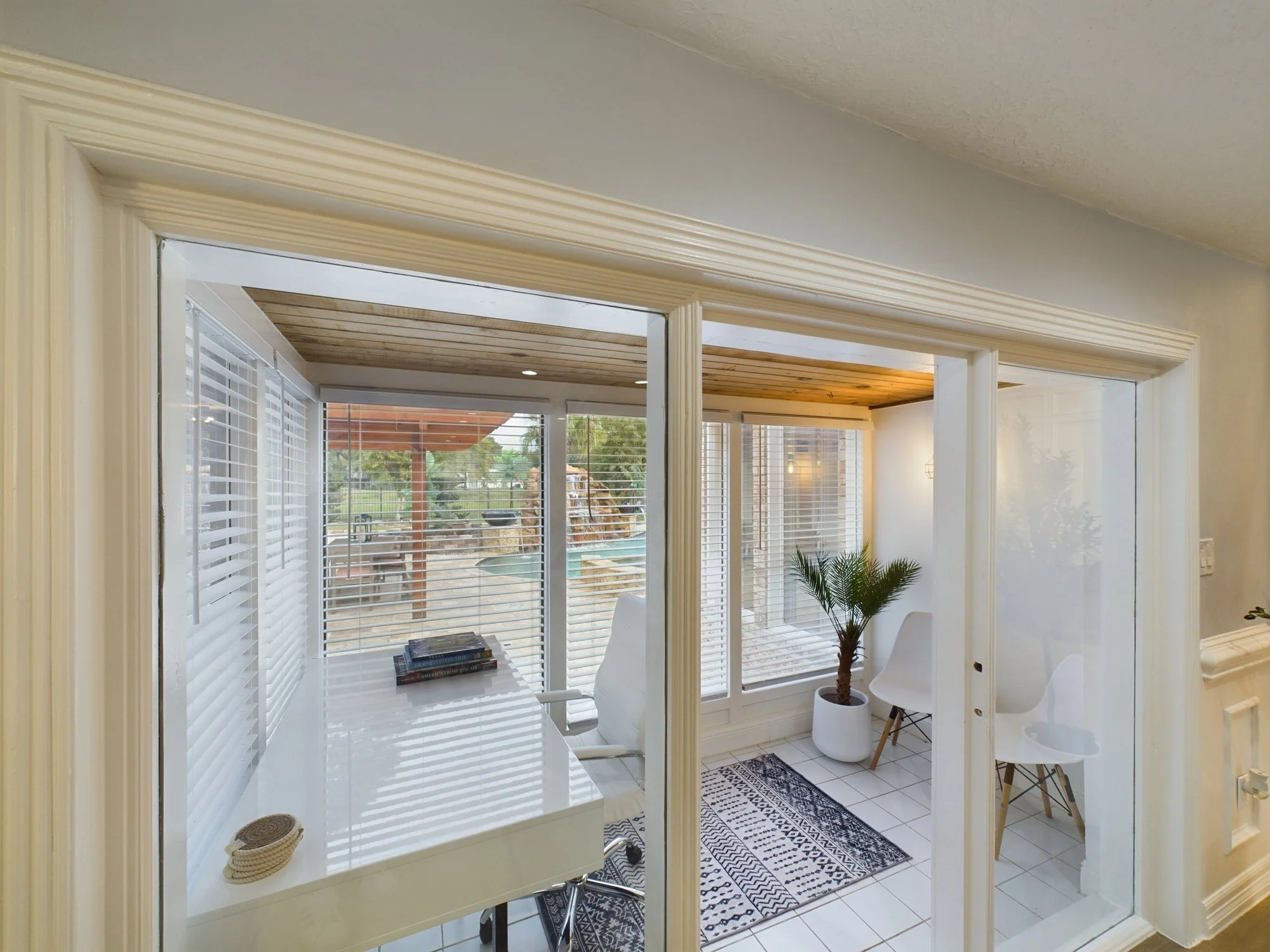 Bright sunroom with large windows, white furniture, and a small indoor plant in a white pot.