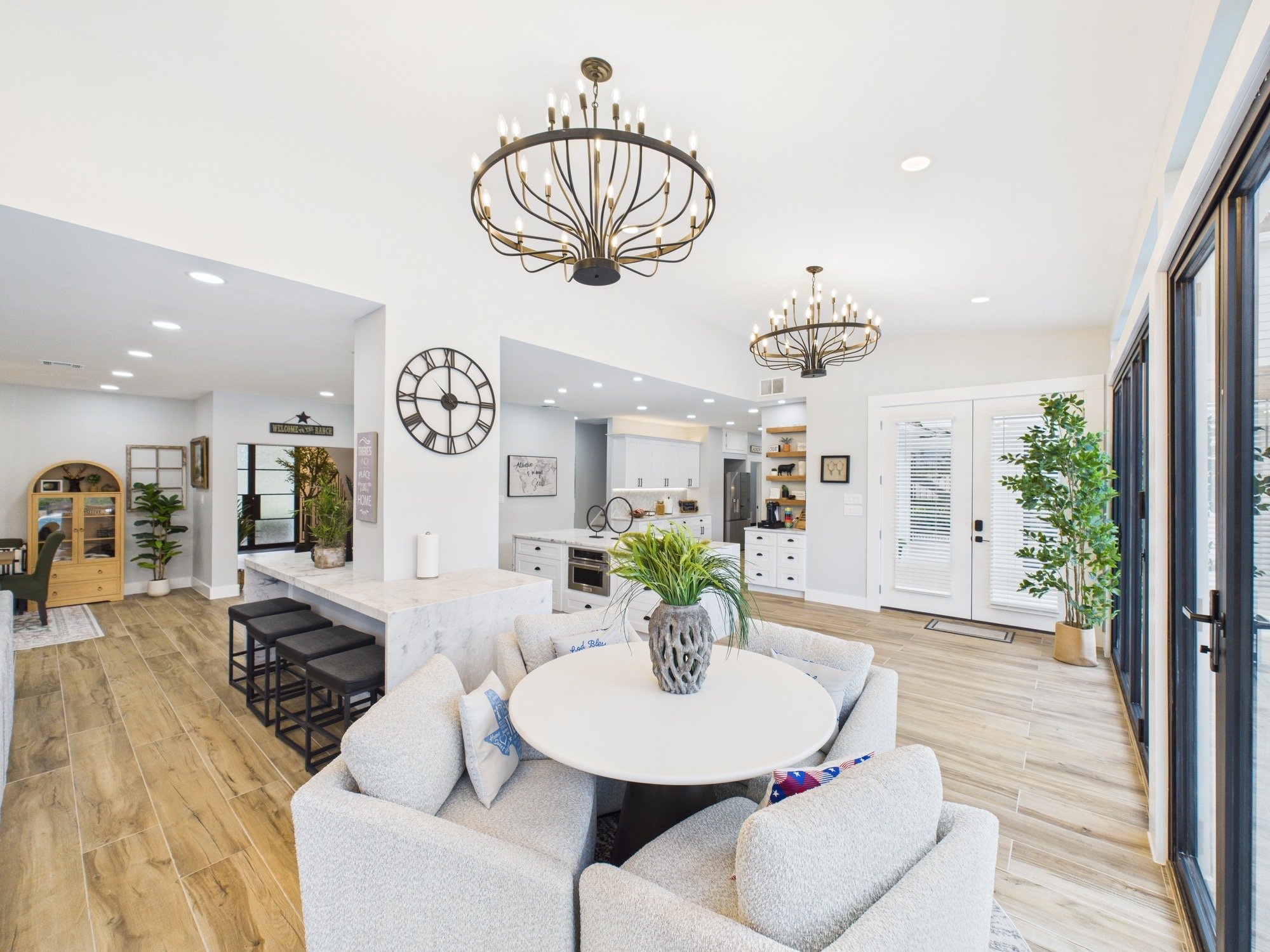 Spacious, modern living room and kitchen with white walls, wood flooring, large windows, and contemporary light fixtures.