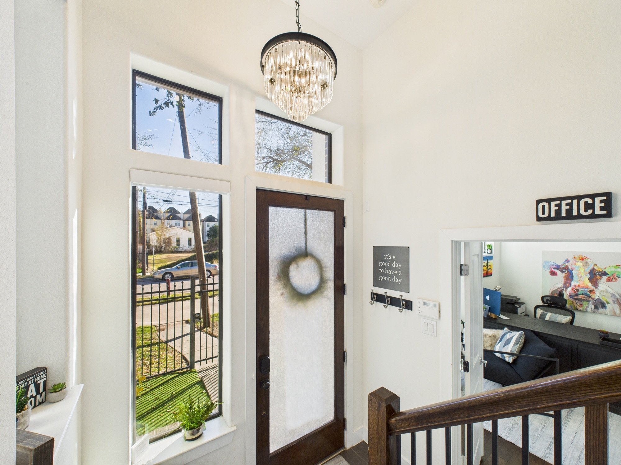 View of inside home entrance with large window over door, small potted plants, and residential neighborhood seen through window.