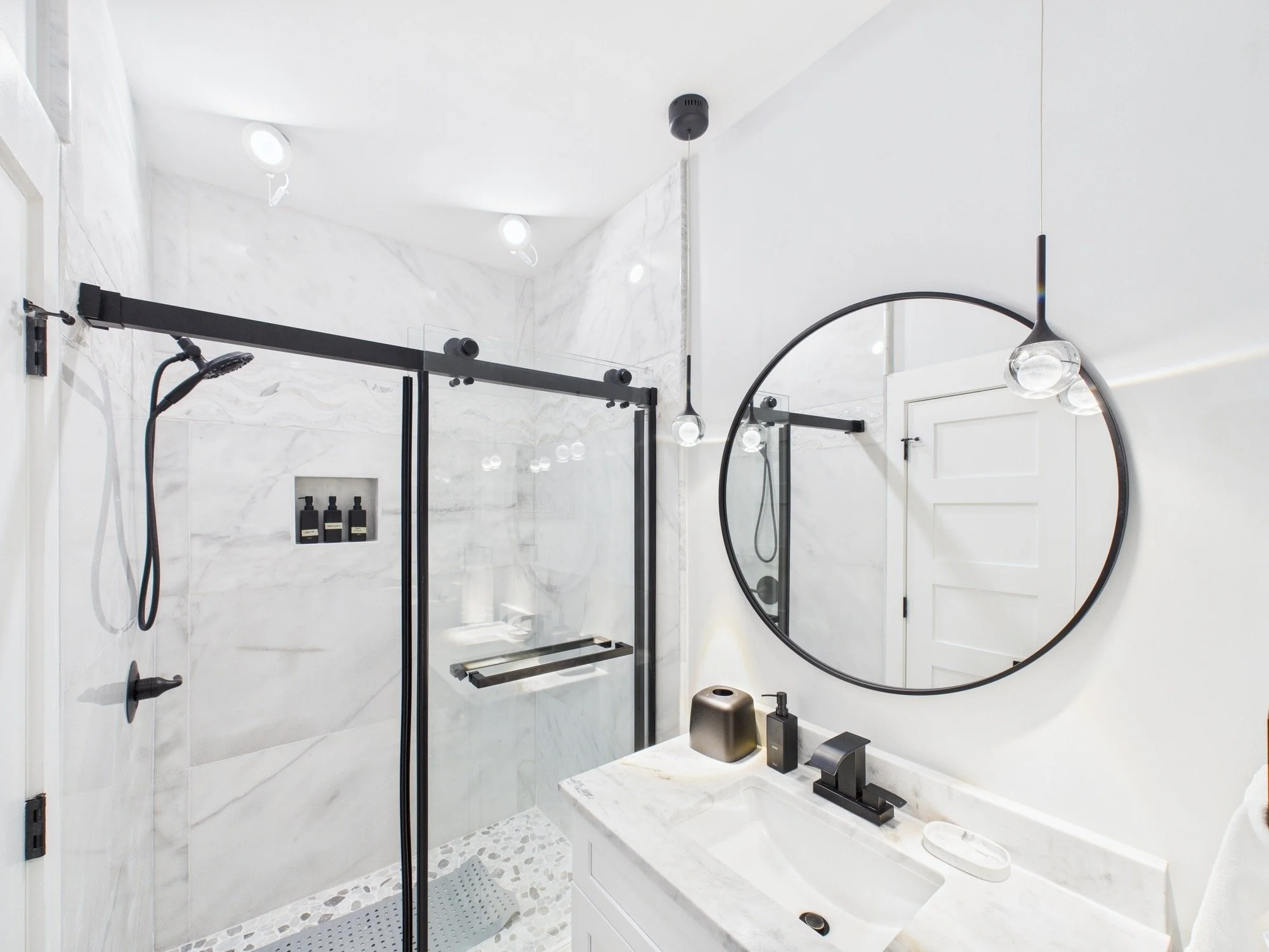 Modern bathroom with marble walls and black fixtures, including a walk-in shower and round mirror.
