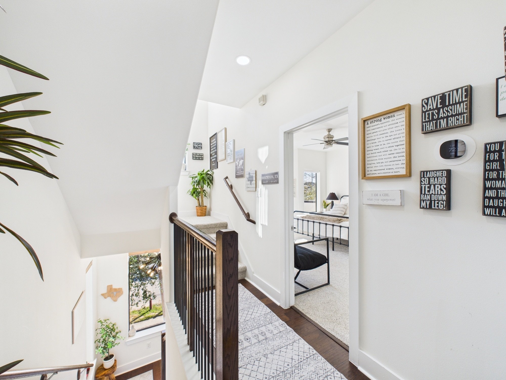 Interior view of a house with a staircase, wall decorations, potted plants, and a sitting area in the background.