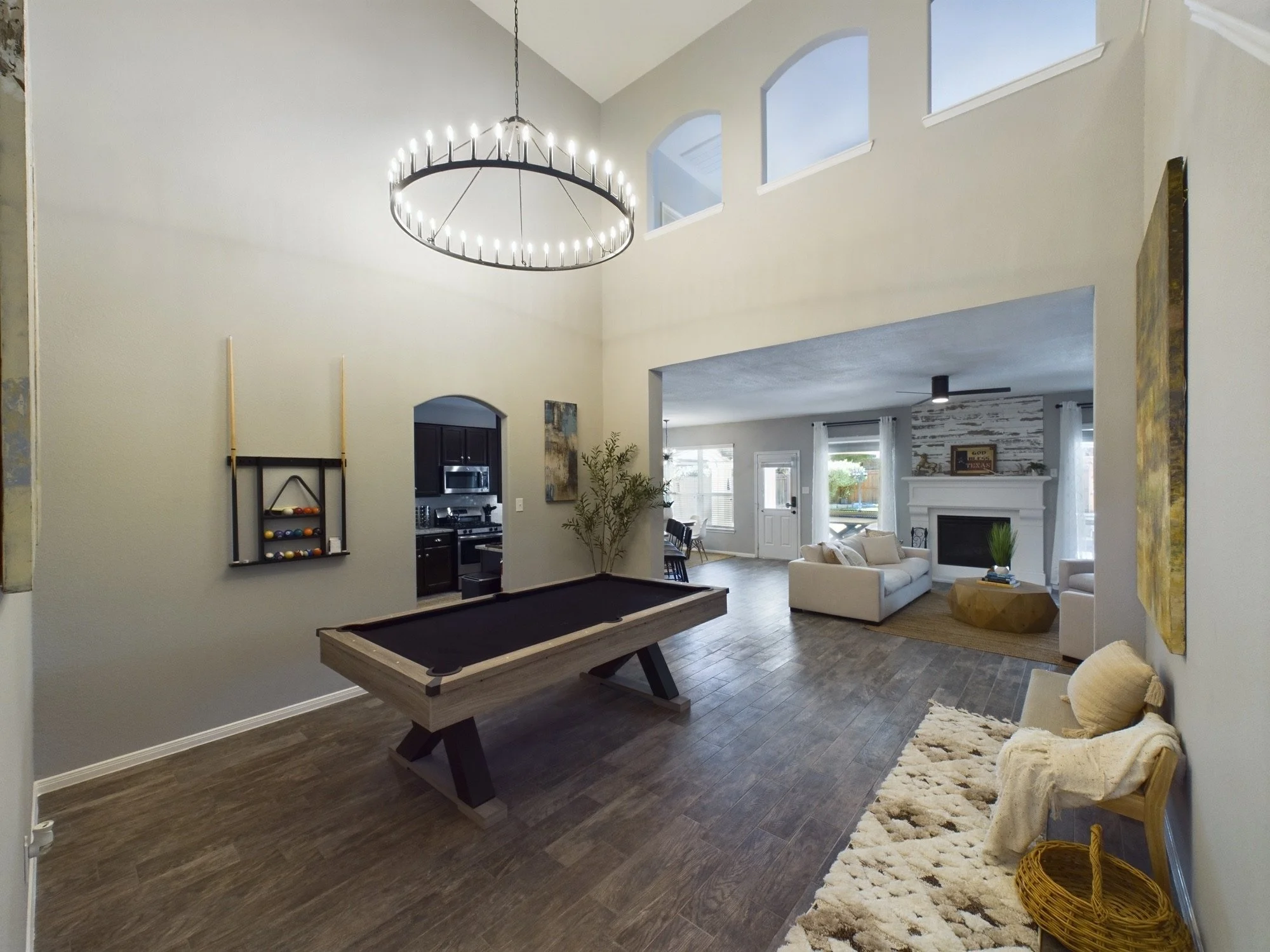 Open-concept living space with high ceilings, large windows, a chandelier, pool table, couch, fireplace, and decorative accents.