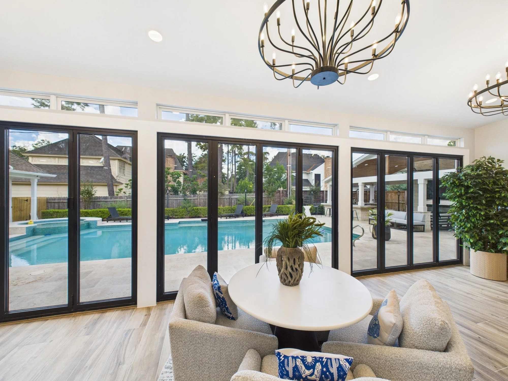 Living room with large sliding glass doors leading to a backyard with a swimming pool, patio, and outdoor seating, illuminated by a modern chandelier with circular light fixtures.