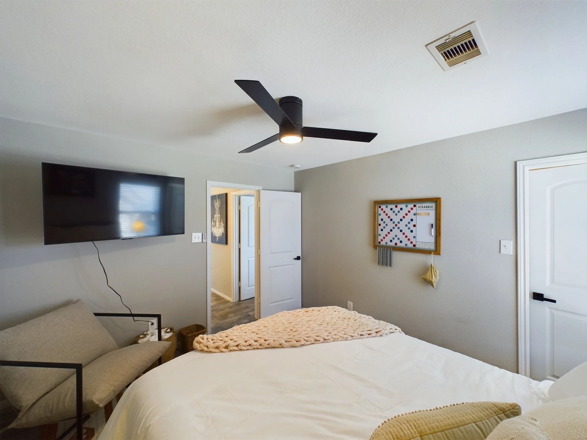 A bedroom with a ceiling fan, a wall-mounted TV, a bed with a knitted blanket, and a door leading to another room.