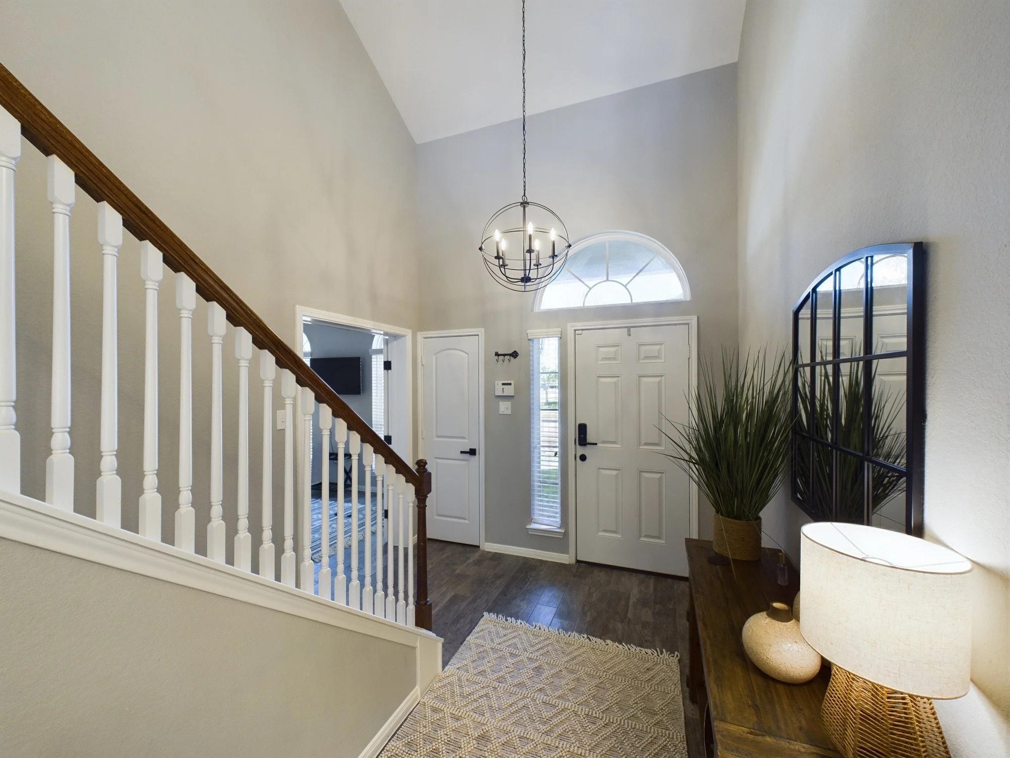 Entryway with front door, high ceiling, chandelier, window, side table, potted plant, and staircase railing.