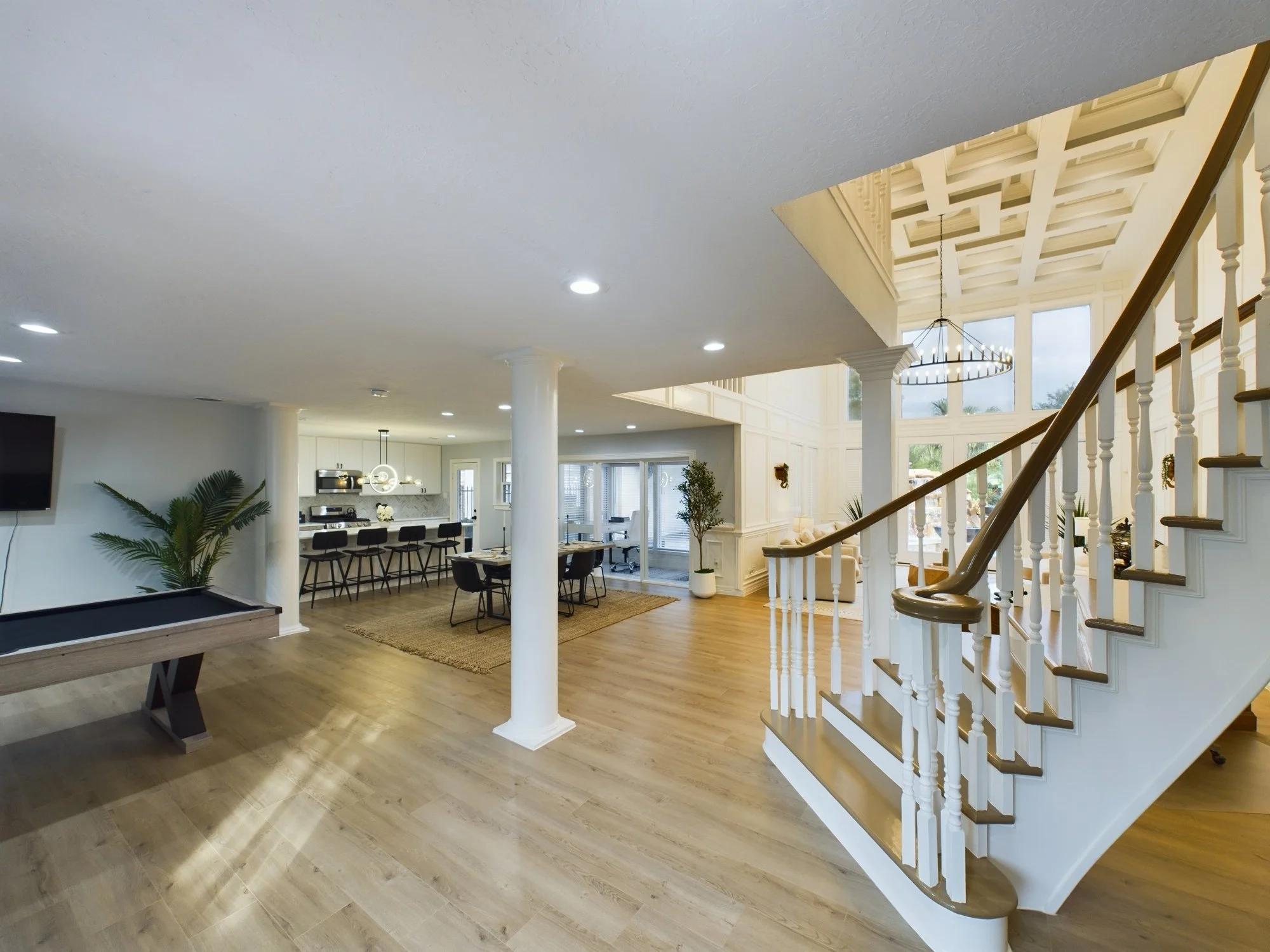 Interior of a modern living room with a staircase, large windows, a dining area, and a pool table.