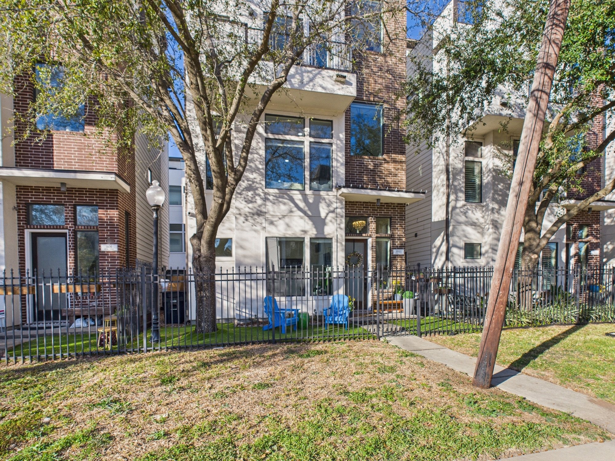 Apartment building with a fenced yard, a tree, and outdoor seating on a sunny day.