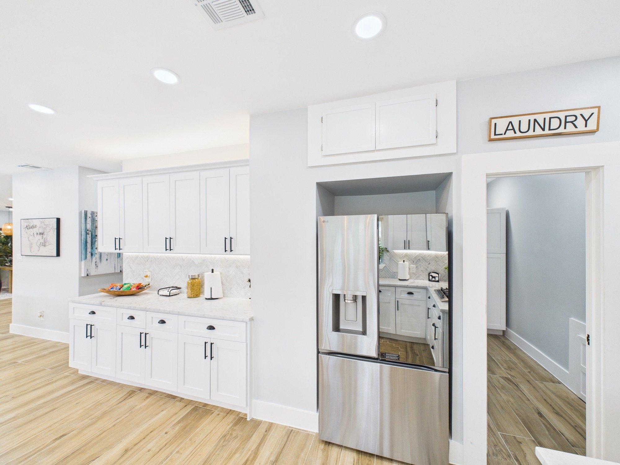 A modern kitchen with white cabinets, a stainless steel refrigerator, and a sign that says "Laundry" on the wall.