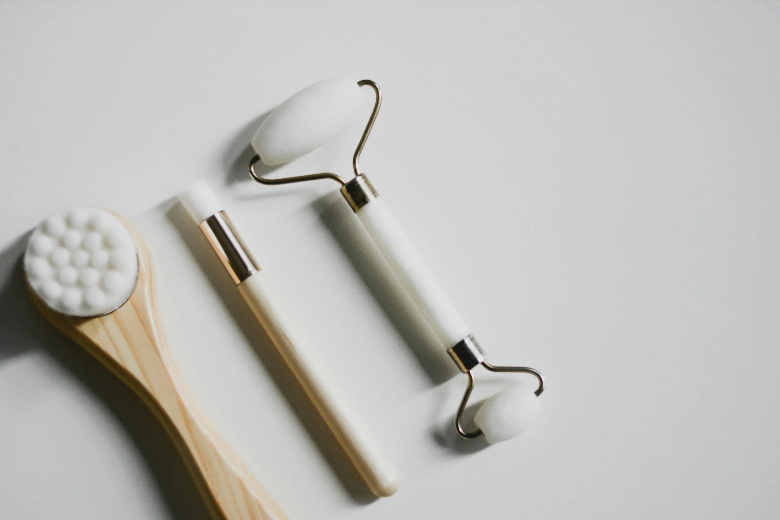 A flat lay of skincare tools including a jade roller, gua sha tool, and a facial roller on a white surface.