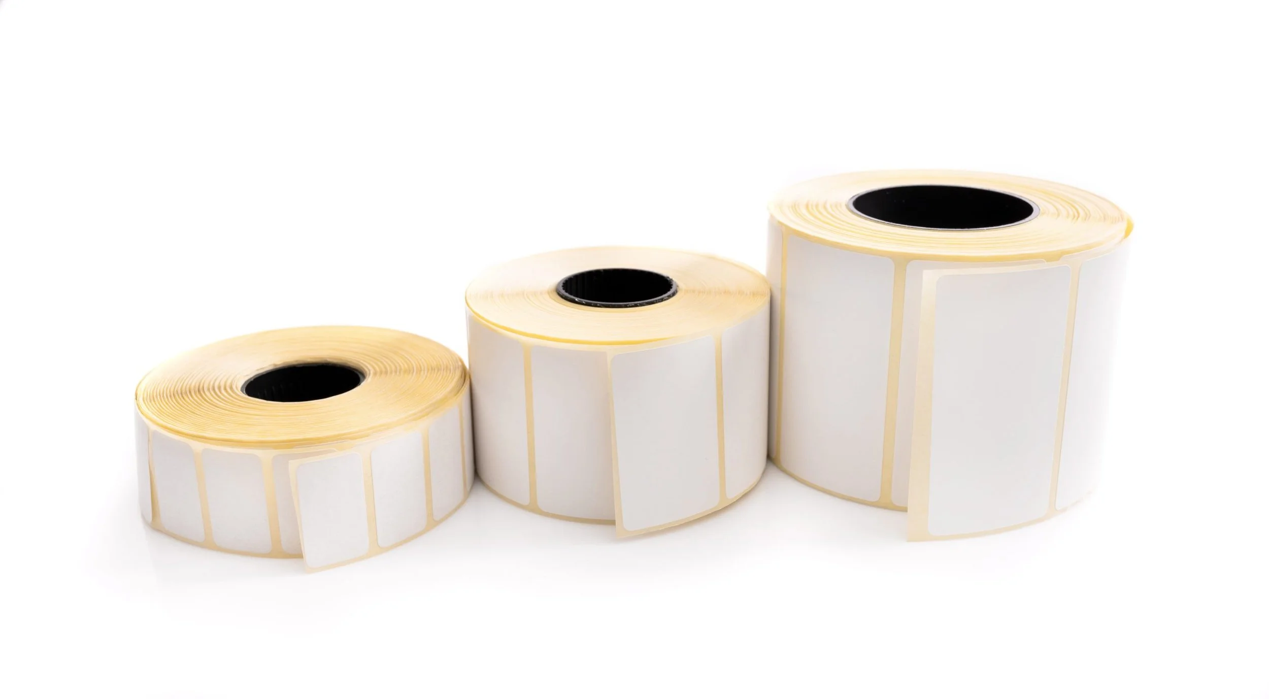 Three rolls of blank label stickers with black center cores, arranged from smallest to largest on a white background.