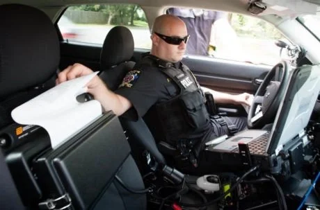 Parking enforcement officer using a mobile e-ticket printer inside a patrol vehicle.