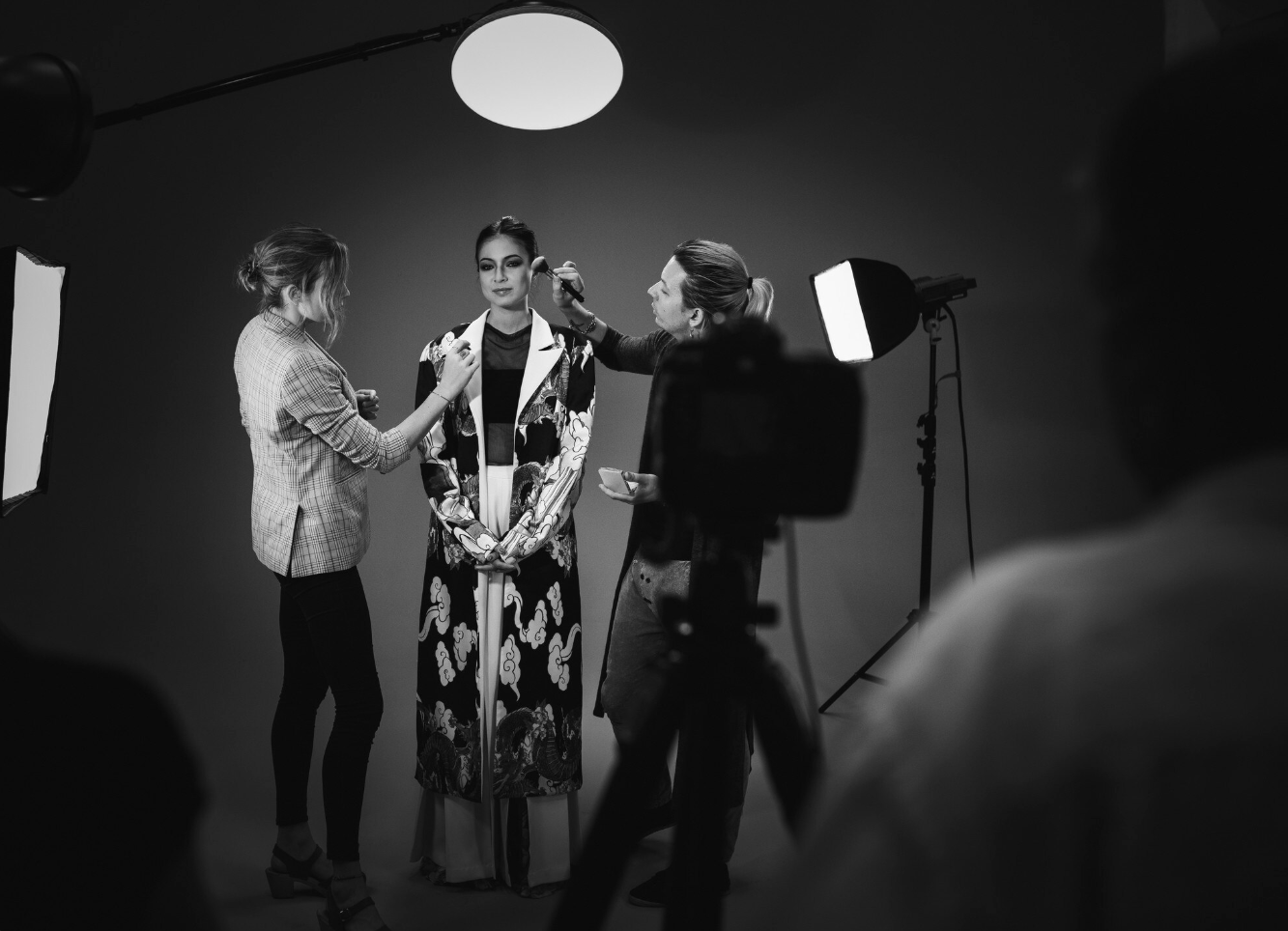 Mujer en set de filmación recibiendo maquillaje y peinado, con equipo de iluminación y cámaras en fondo