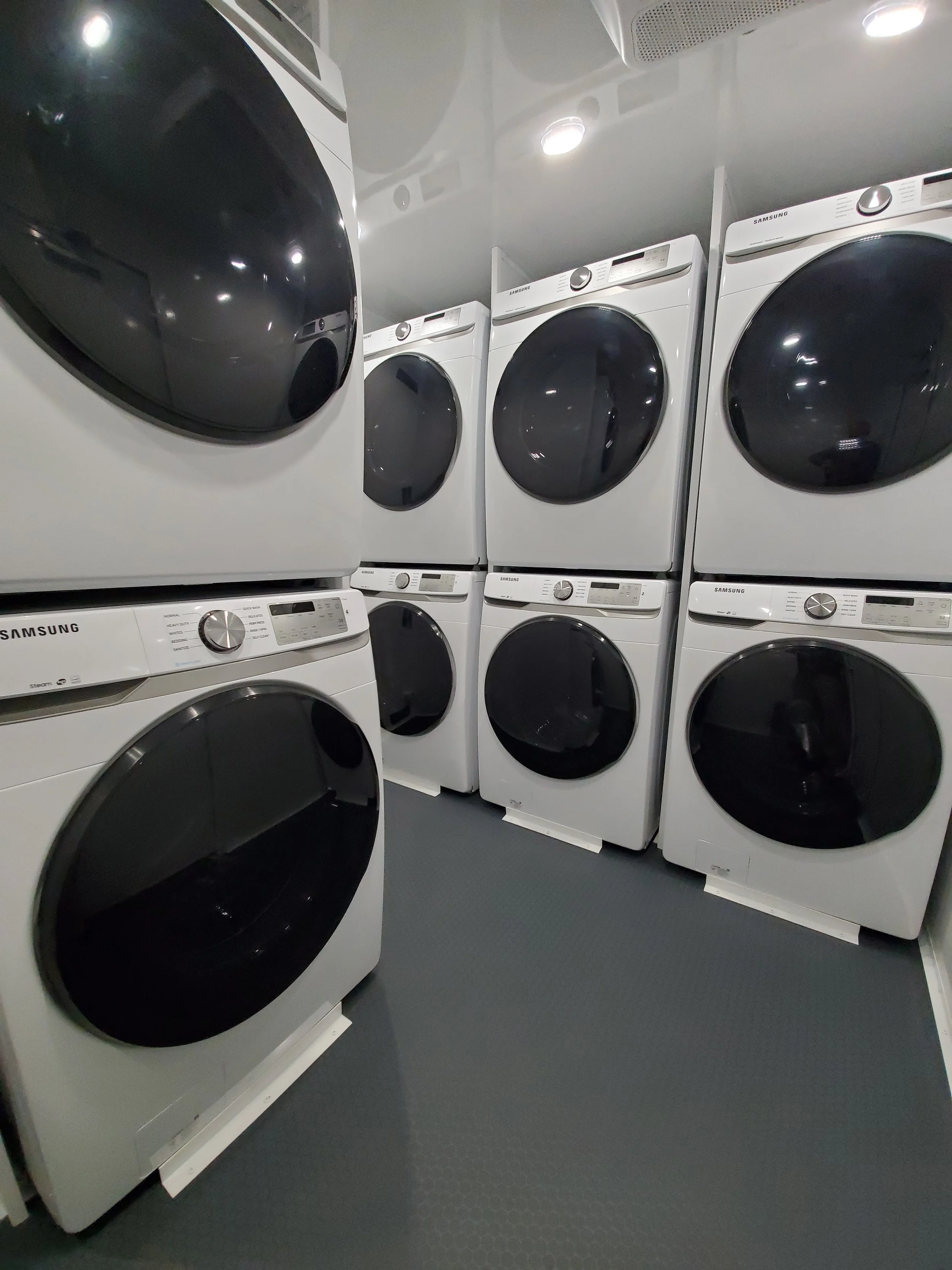 A room with multiple stacked white Samsung front-loading washing machines and dryers with black doors.