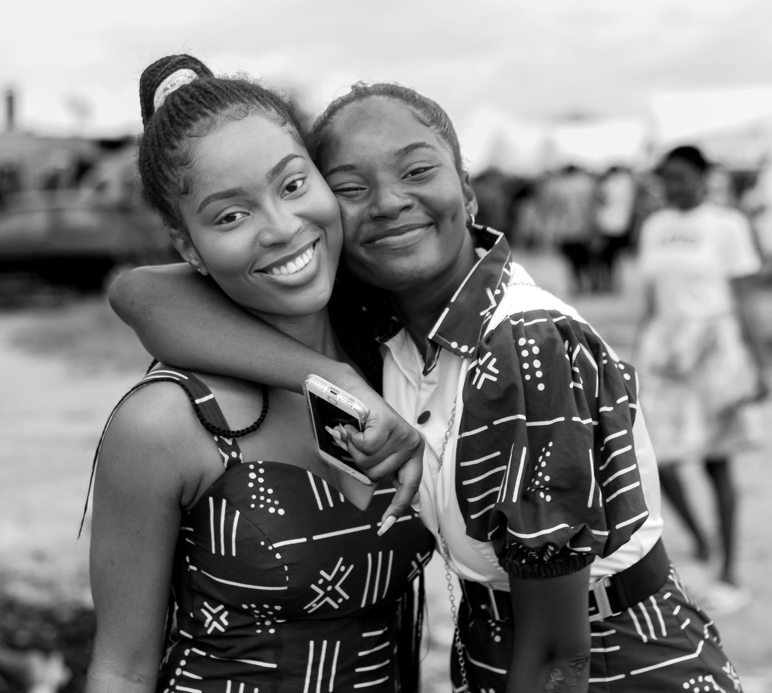 Two women hugging each other with smiling faces, outdoors, black and white photograph.