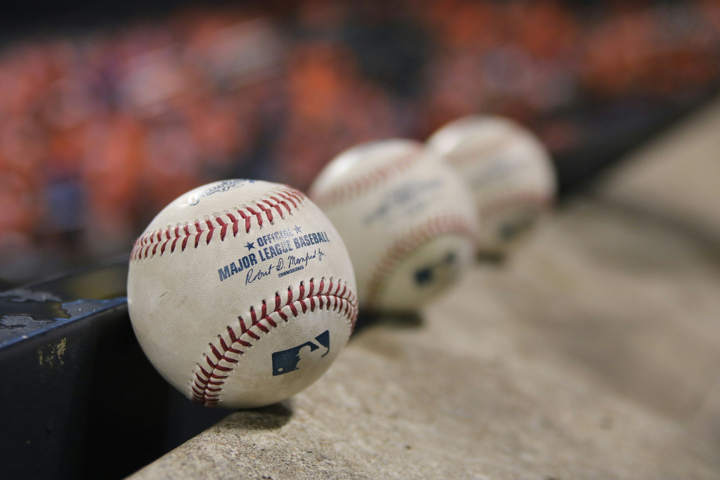 Close-up of three baseballs lined up on a surface, with a blurred background of baseball stadium seating.