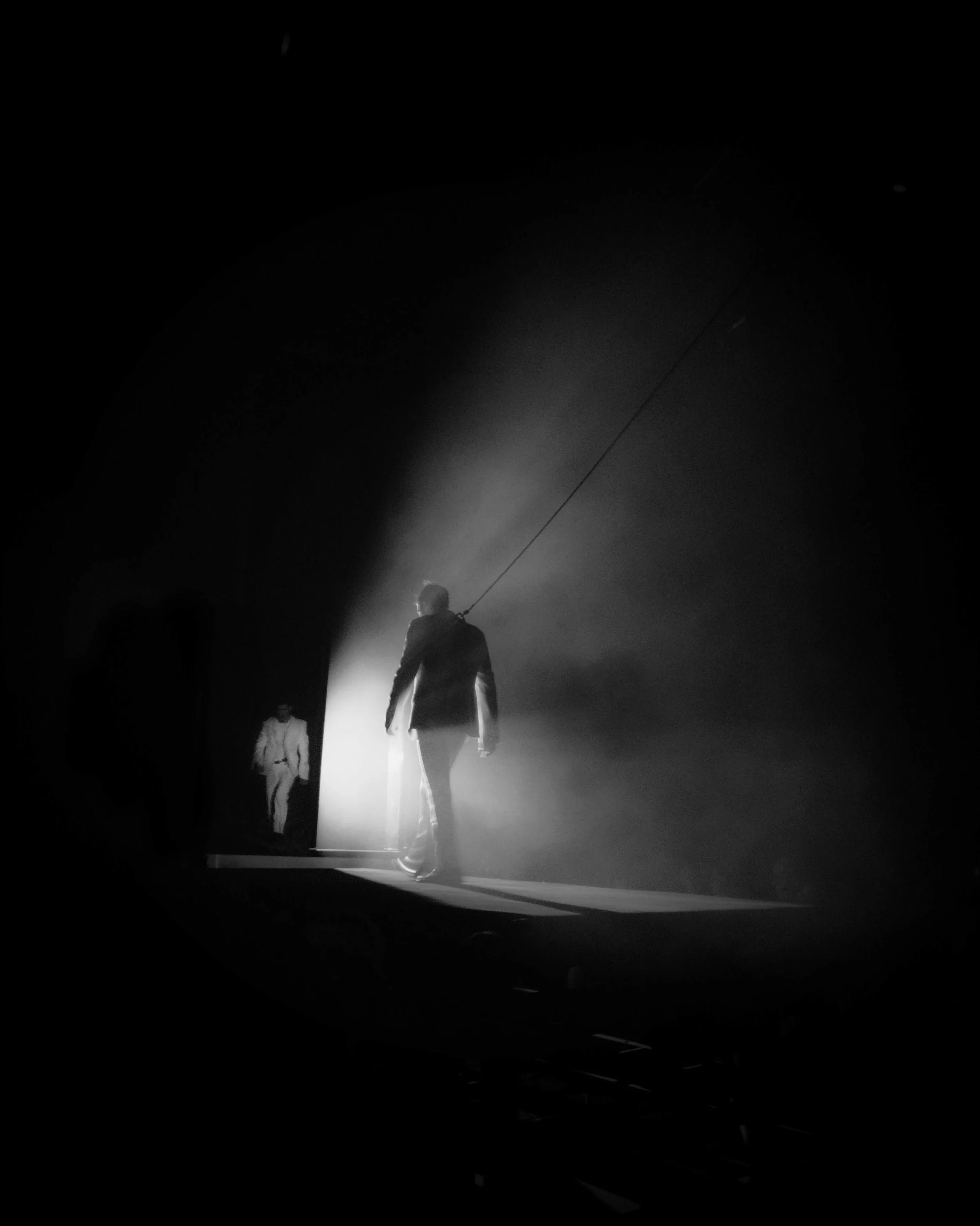 Man walking through a dark tunnel with bright light shining behind him, other figures visible in the background.
