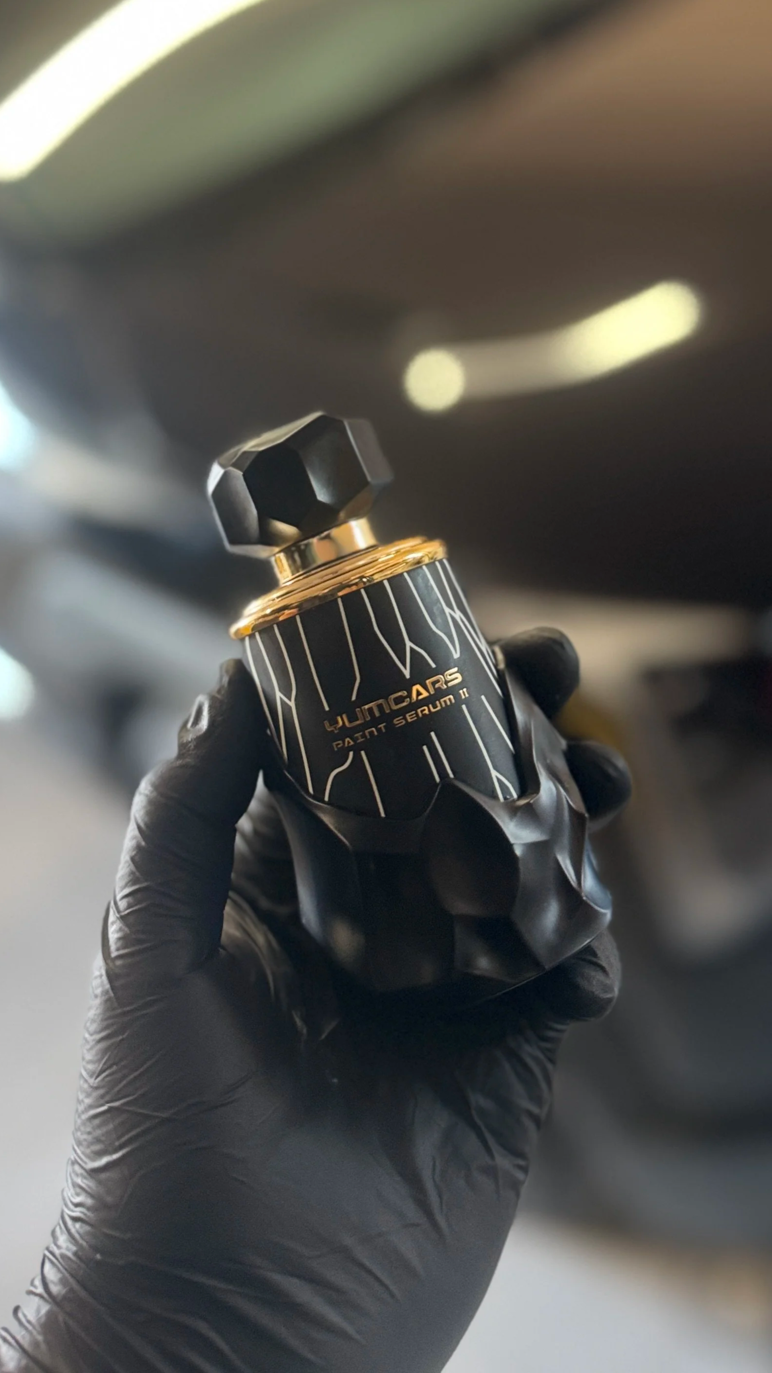 A gloved hand holding a small black and gold container labeled 'WUNCARS Paint Serum II'.