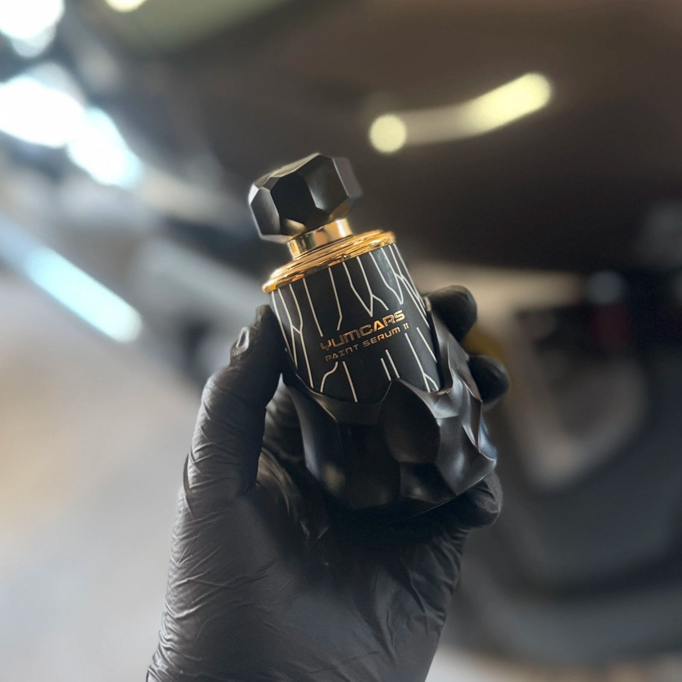 Close-up of a gloved hand holding a cosmetic tube with a black cap and gold accents.
