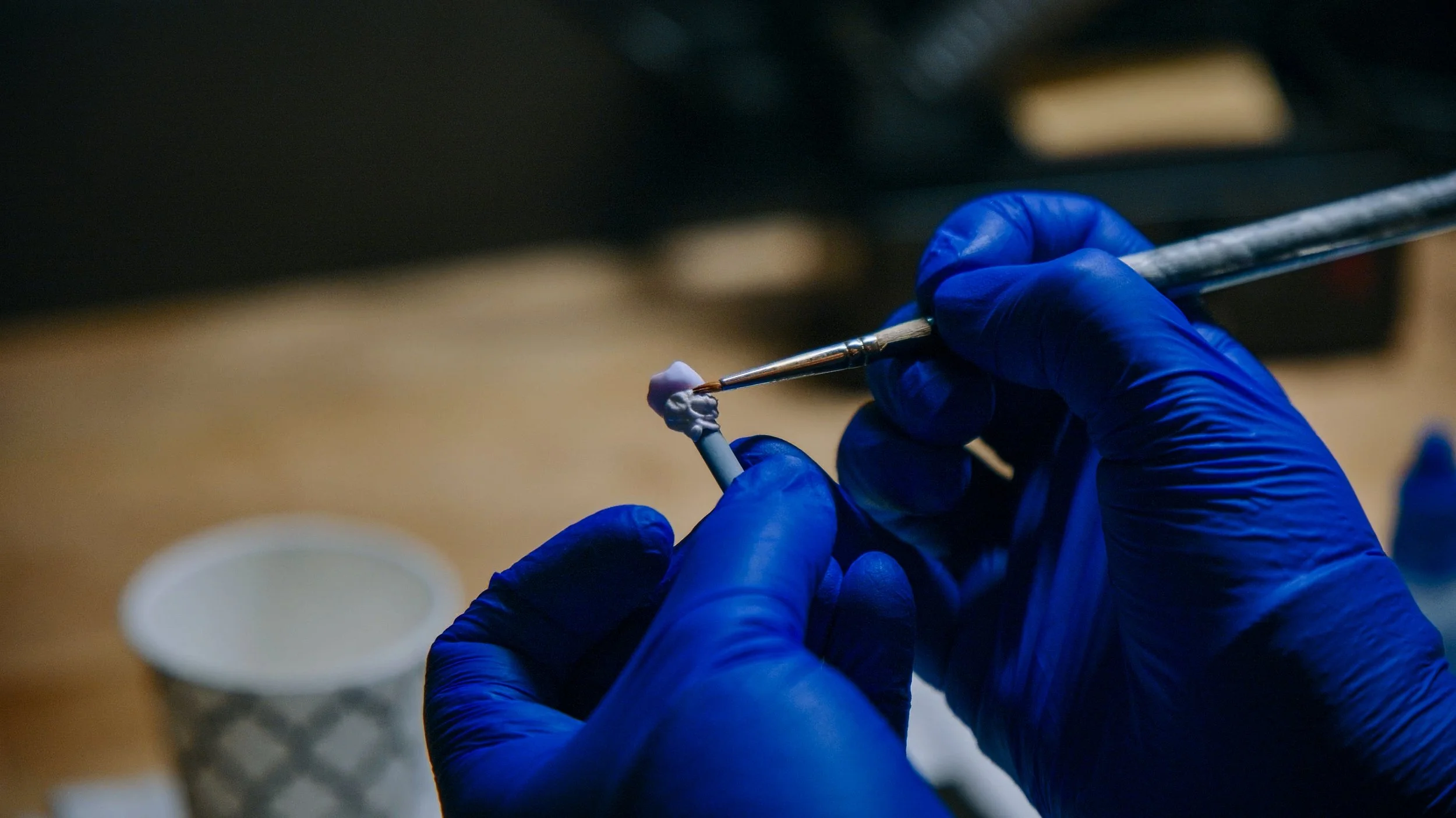 A person wearing blue gloves holding a dental tool and working on a small model of teeth.
