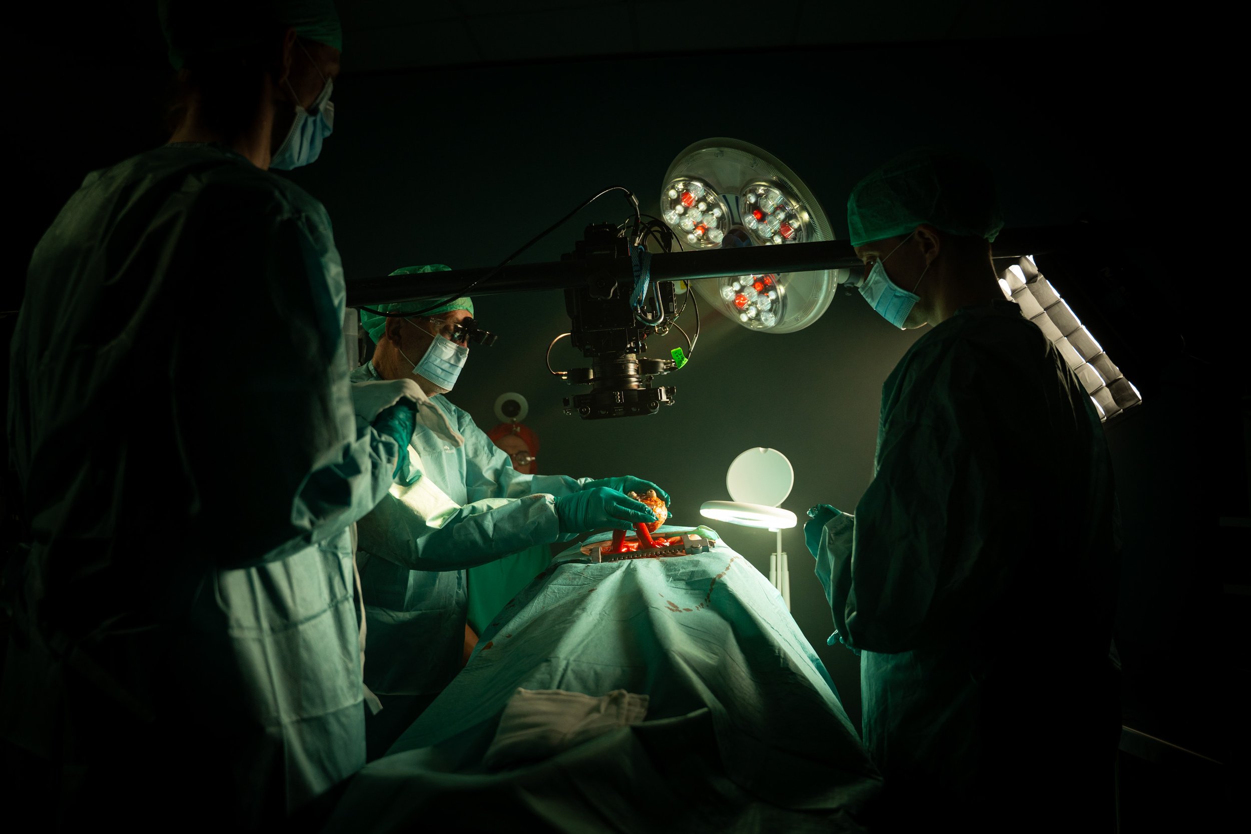 Surgeons performing an operation in an operating room under bright surgical lights, wearing surgical masks and gowns.