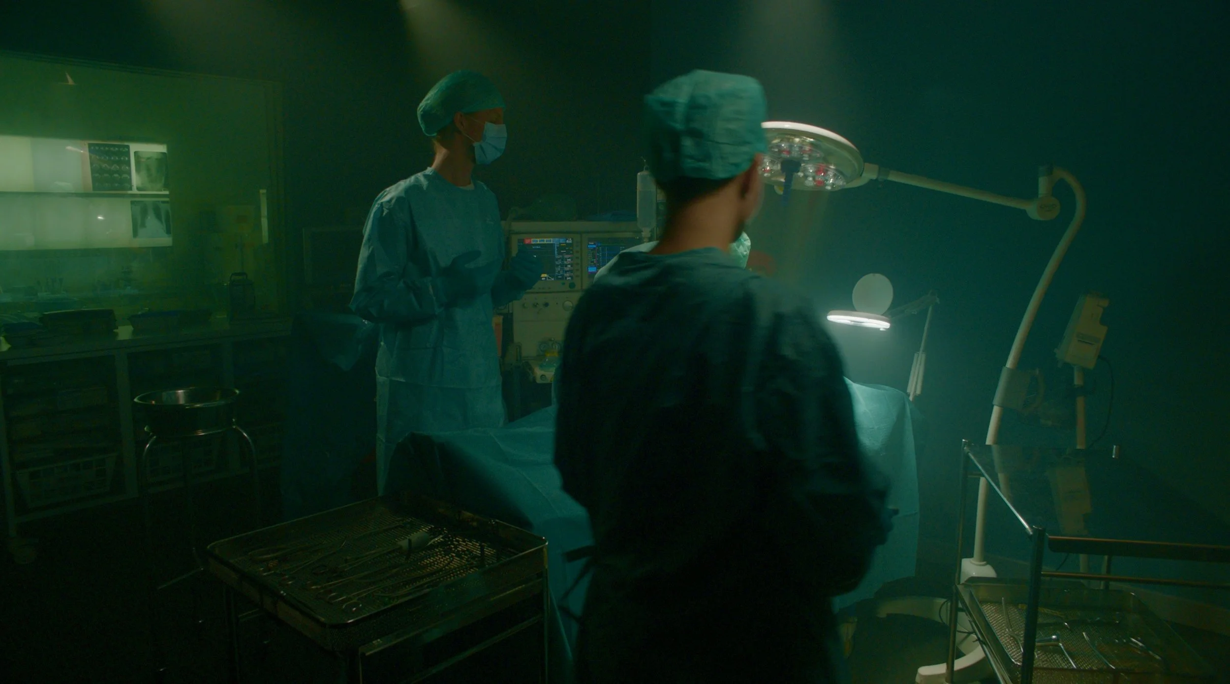 Medical team in an operating room performing surgery, with two surgeons, screens, and medical equipment.