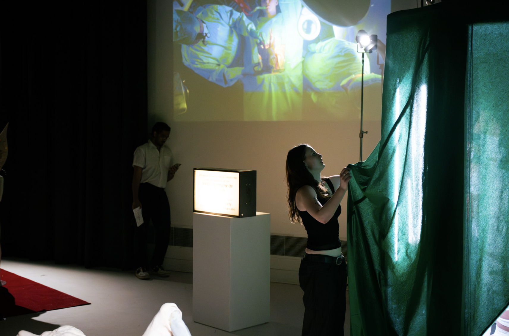 A woman is pulling back a green curtain to reveal a projection of an underwater scene with divers on a screen at an indoor exhibition or event.